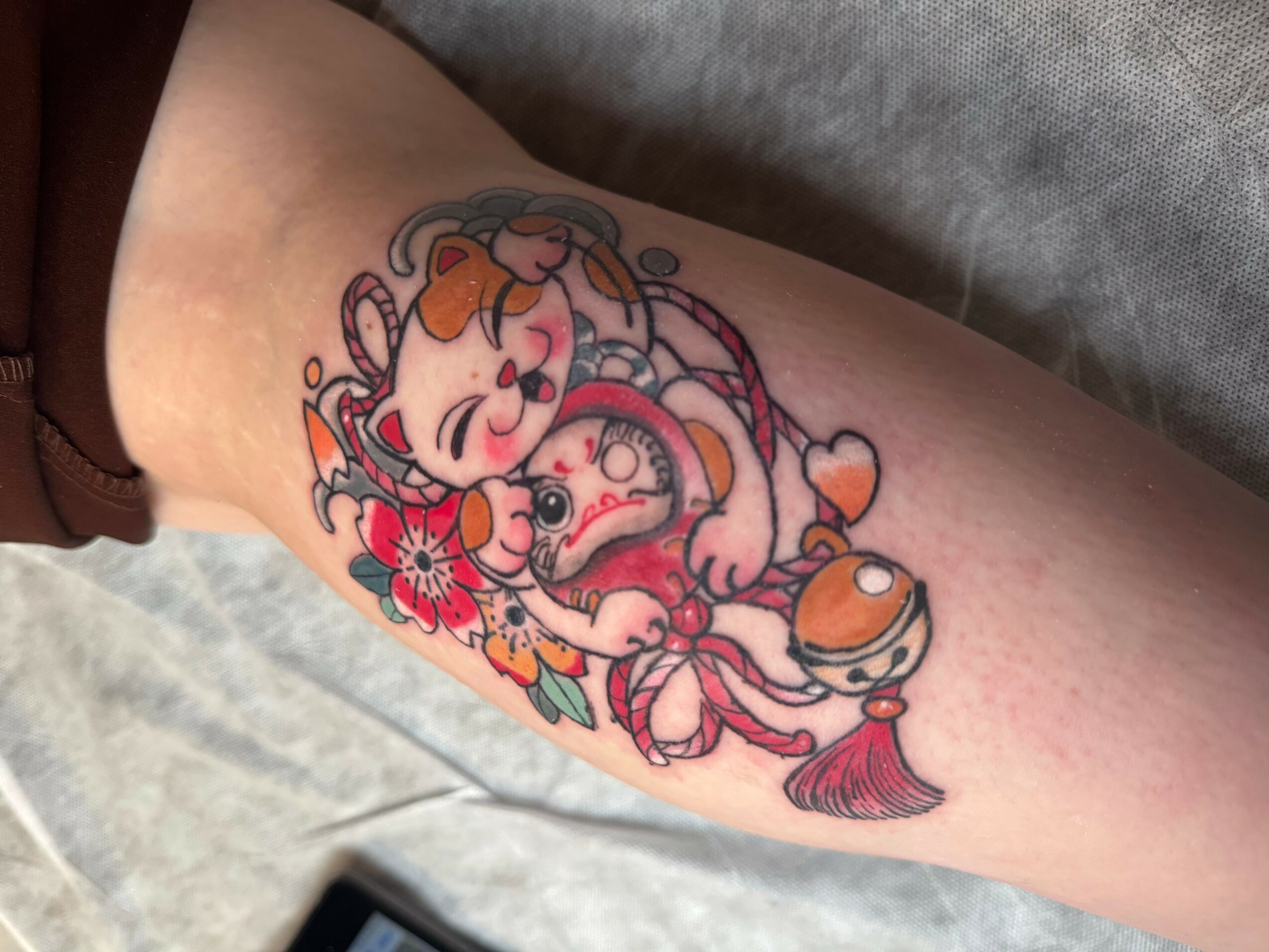 Tattoo of a girl with a bow, surrounded by flowers and a small animal, on a person's thigh.
