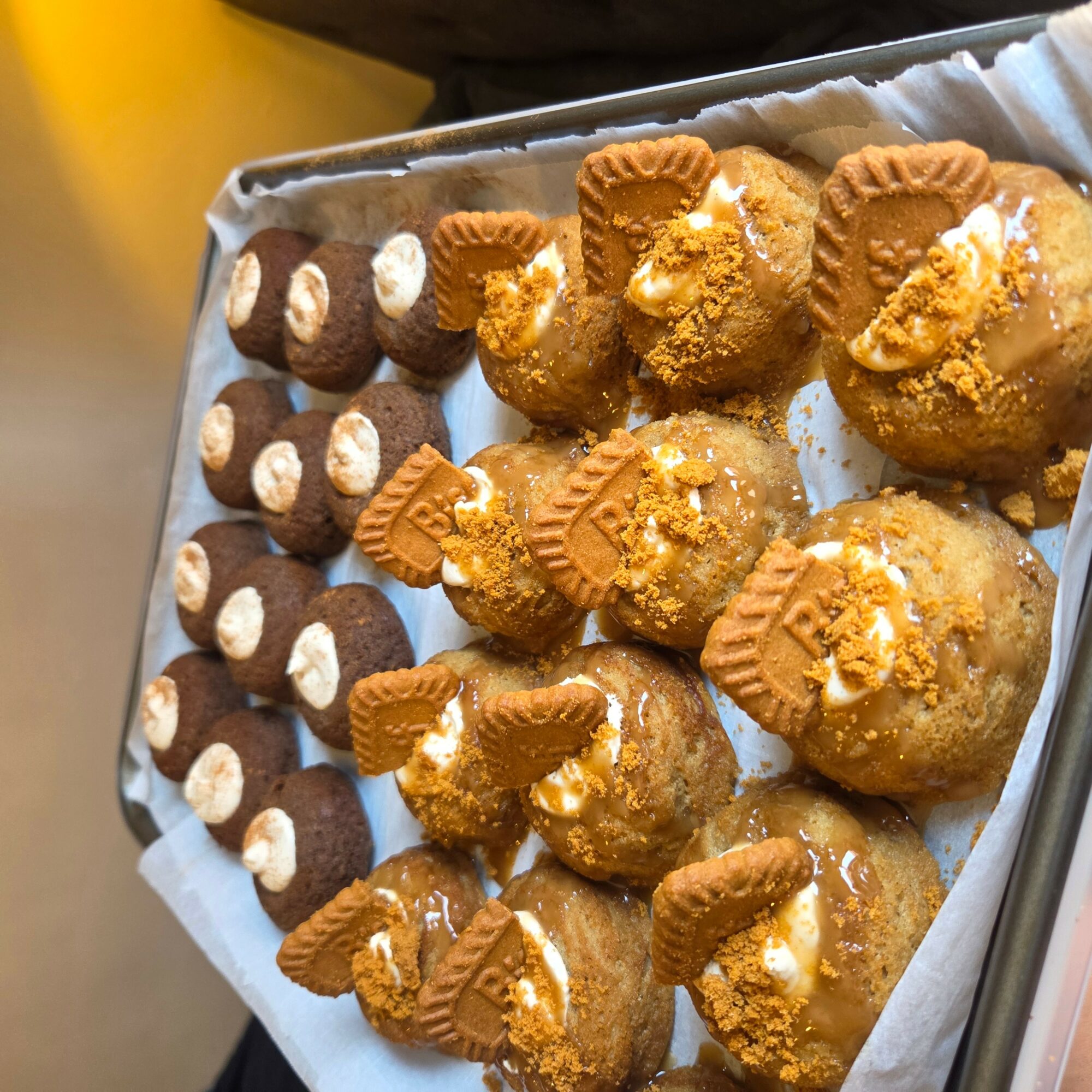 Tray of round desserts topped with cookies and crumbles, lined with parchment paper, viewed from above.