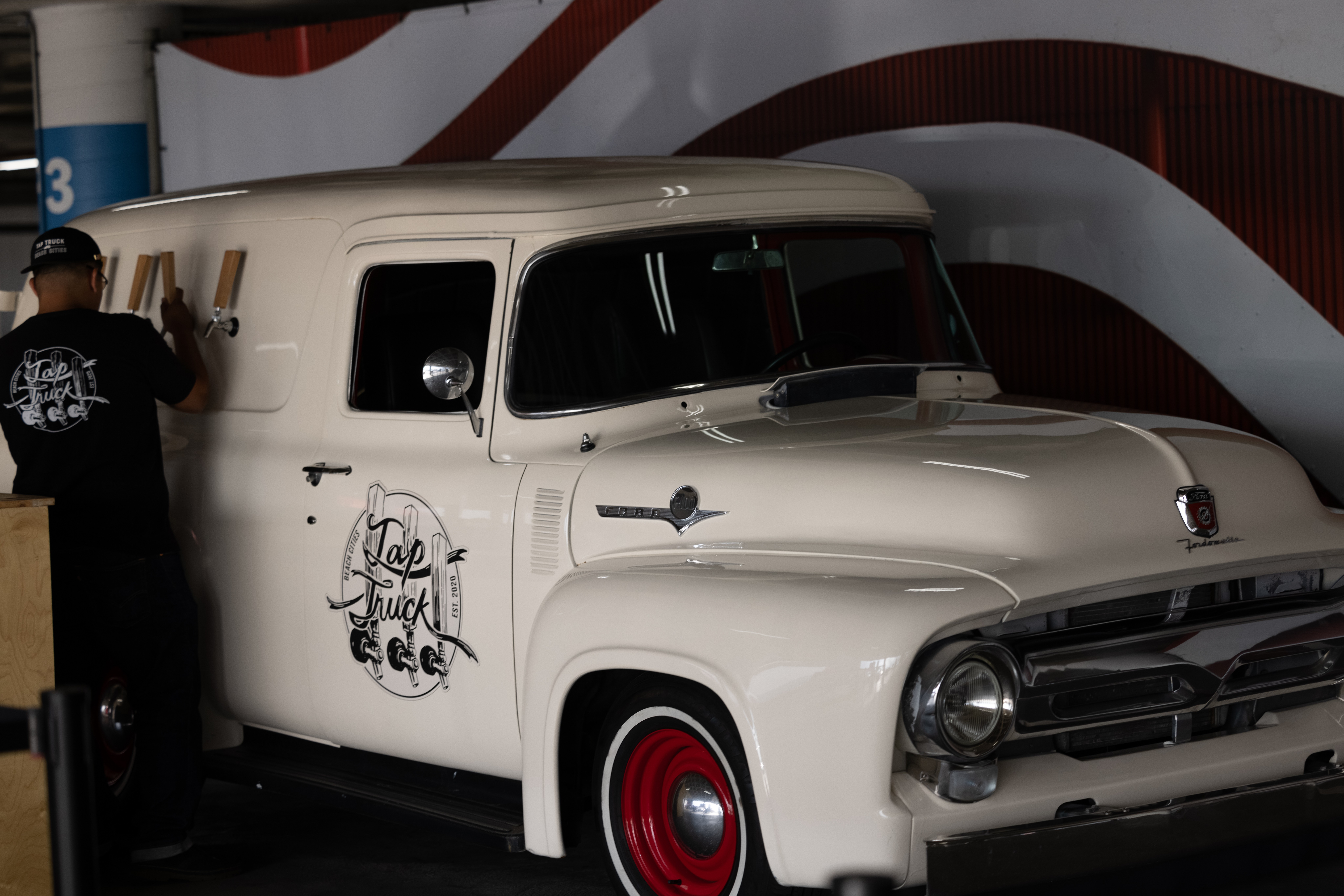 Person standing next to a vintage white delivery van with red wheels, inside a building with a curved wall.