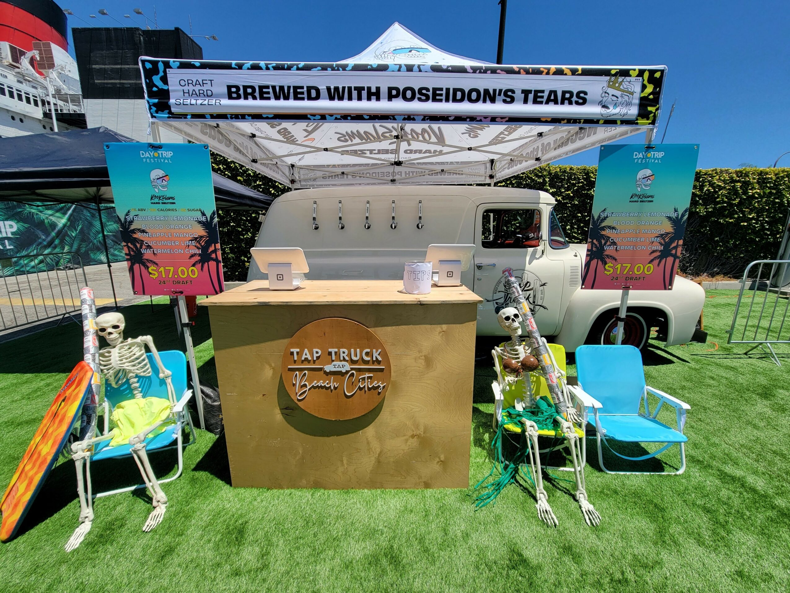 Brewed with Poseidon's Tears sign on tent, two skeleton figures on chairs, and a tap truck setup outdoors.