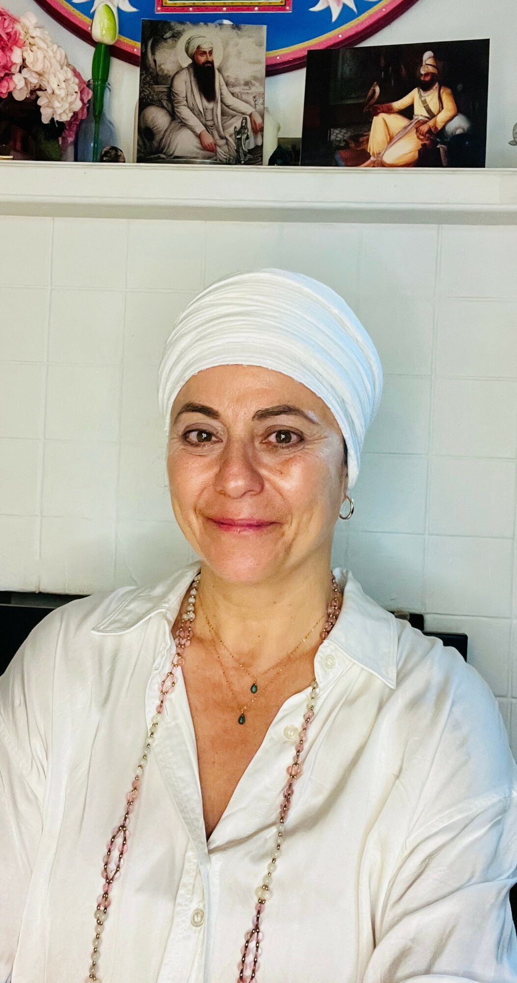 Woman wearing a white headscarf and white shirt, smiling, with framed pictures above her head.