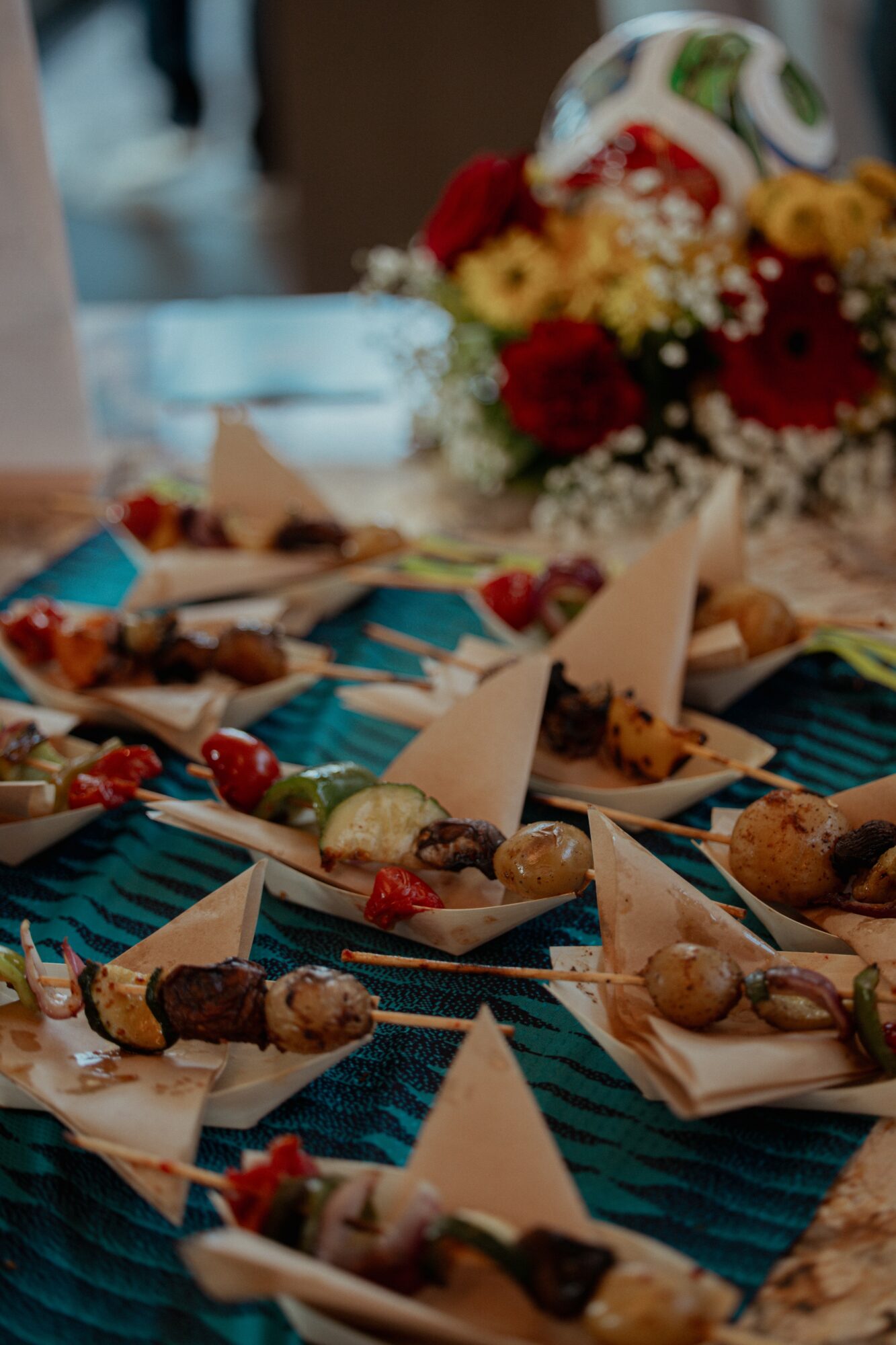 Assorted appetizers on a table with a colorful flower arrangement in the background.
