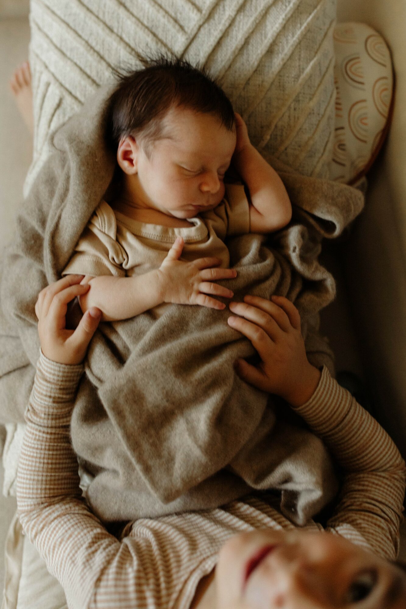 A sleeping baby wrapped in a blanket, held by an adult with striped sleeves, lying on a pillow.