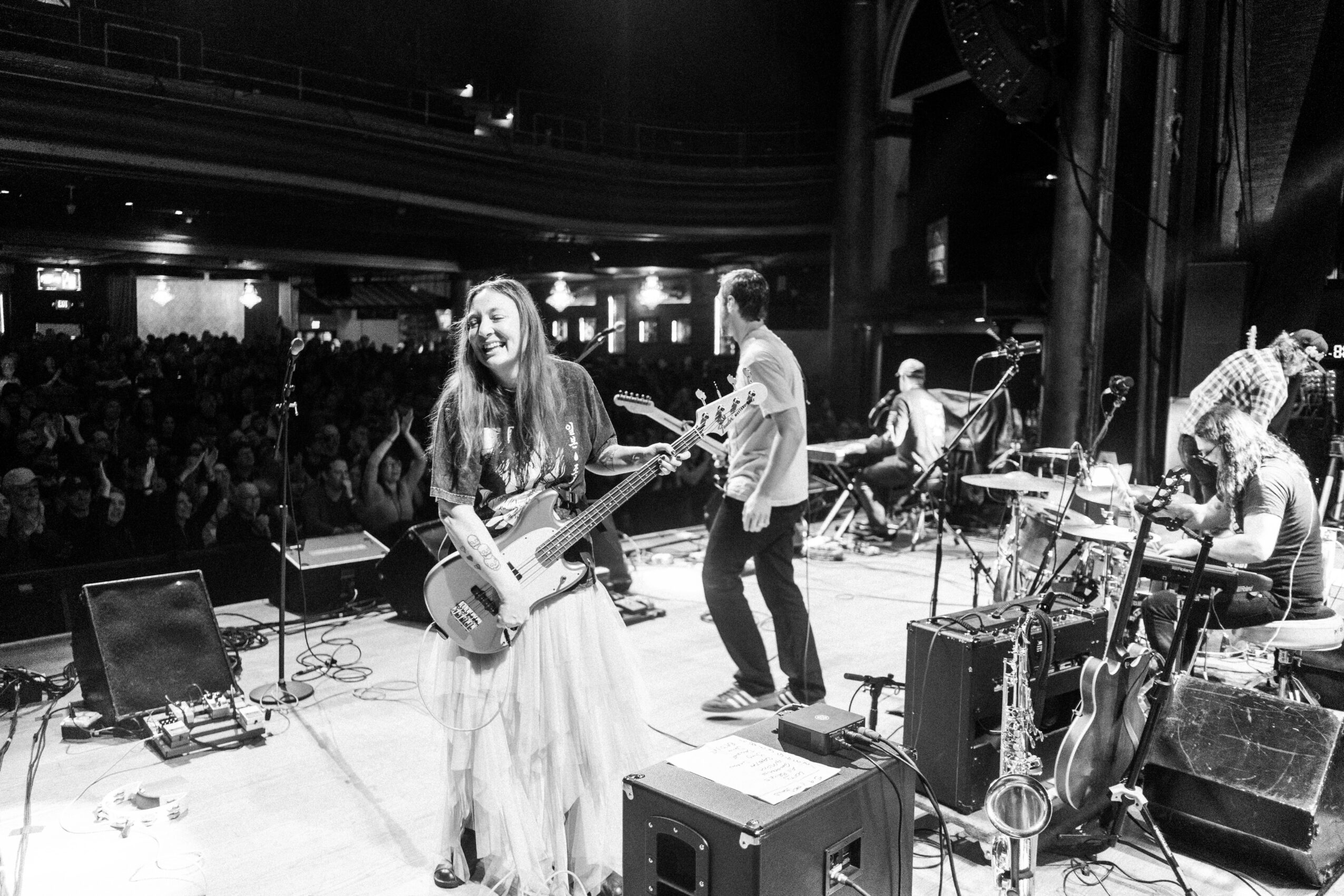 Band performs on stage with a crowd in the background, black and white photo, musicians playing instruments, audience watching.