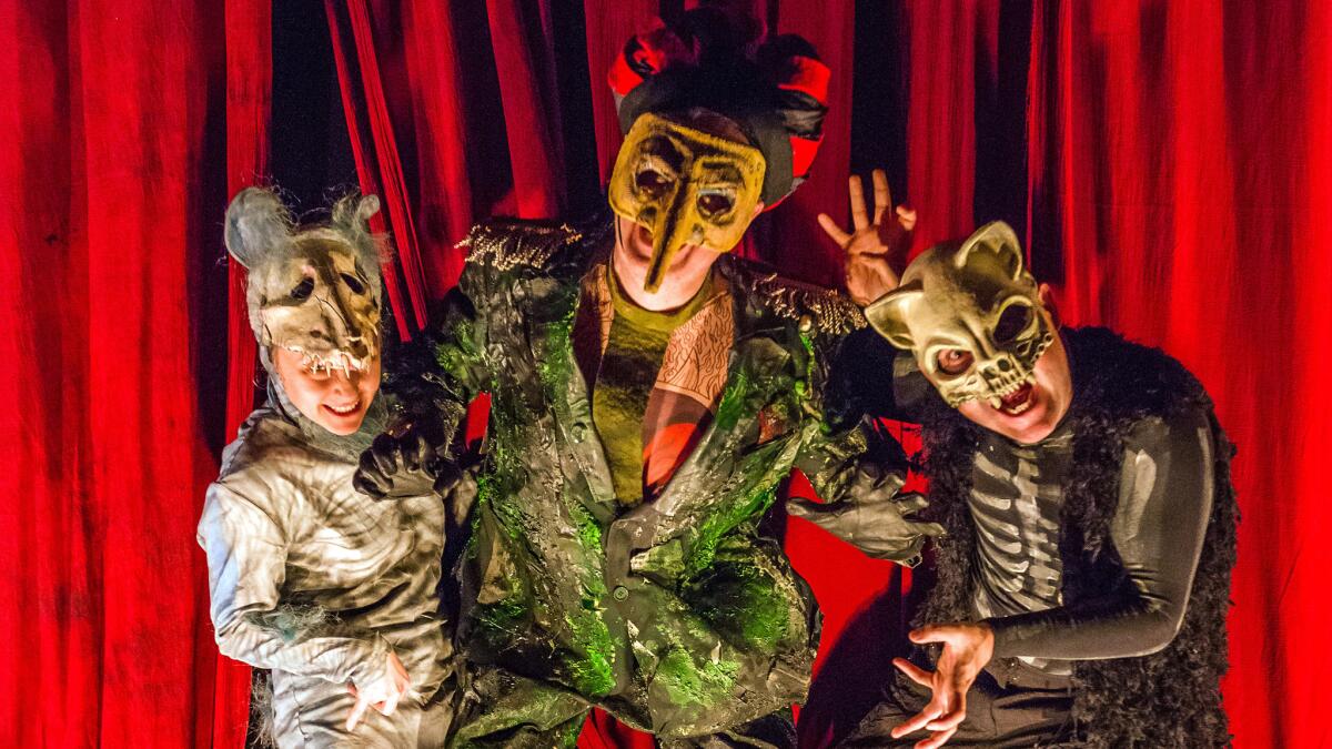 Three performers in costumes and masks on stage with red curtains in the background.