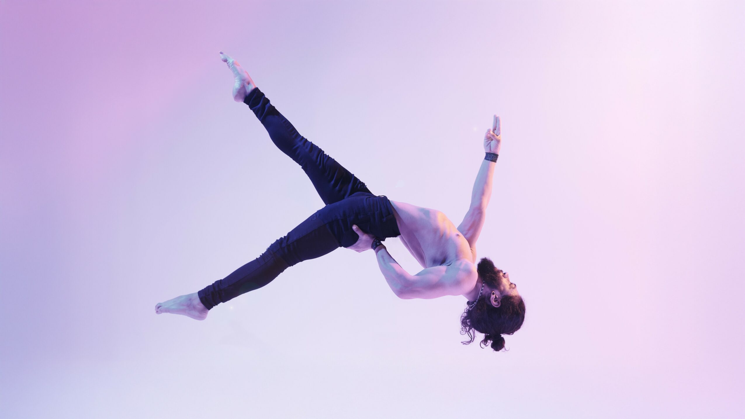 A person performing a mid-air dance or gymnastics move against a gradient background.