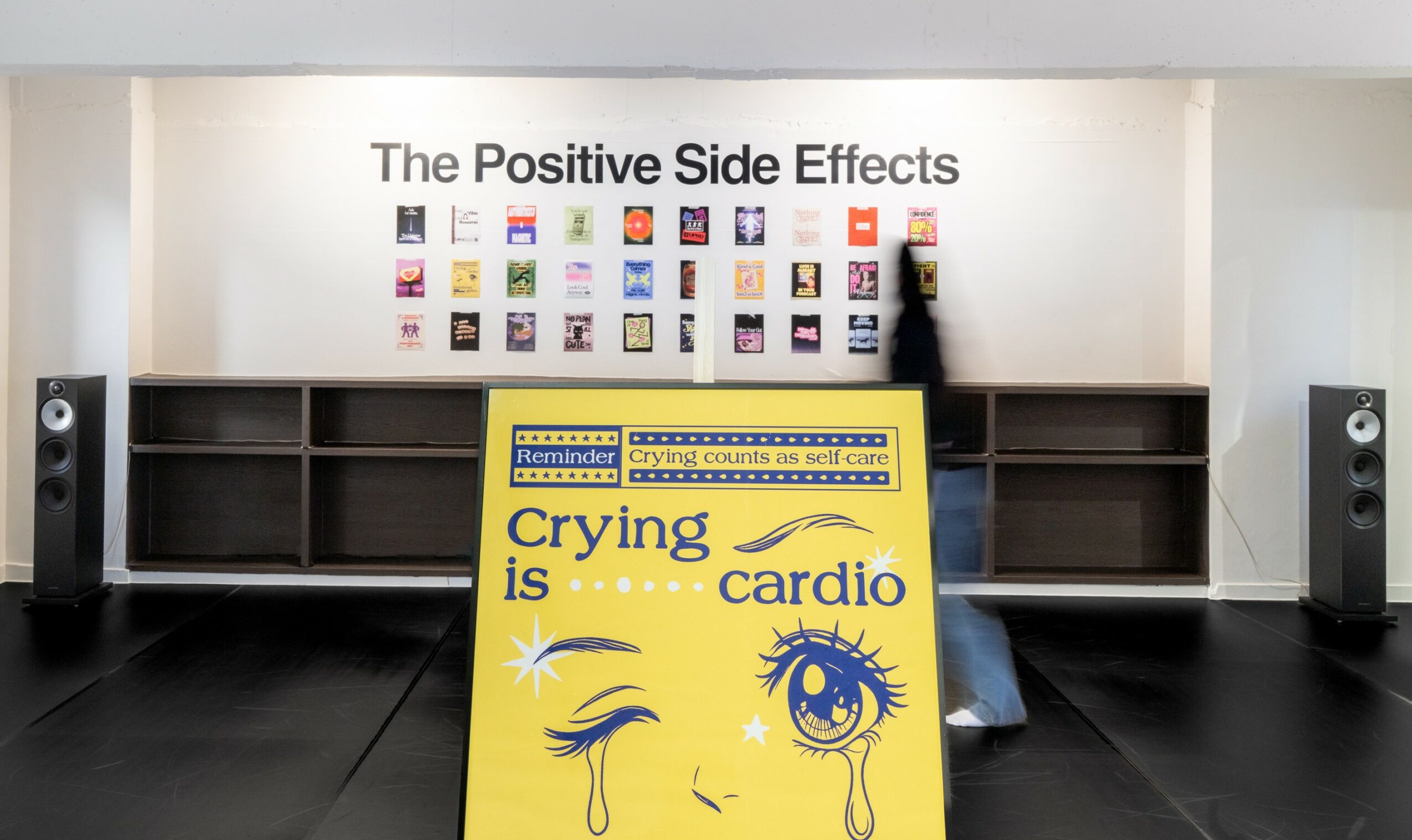 Display with a yellow sign about crying and cardio, and a wall with books and speakers in the background.