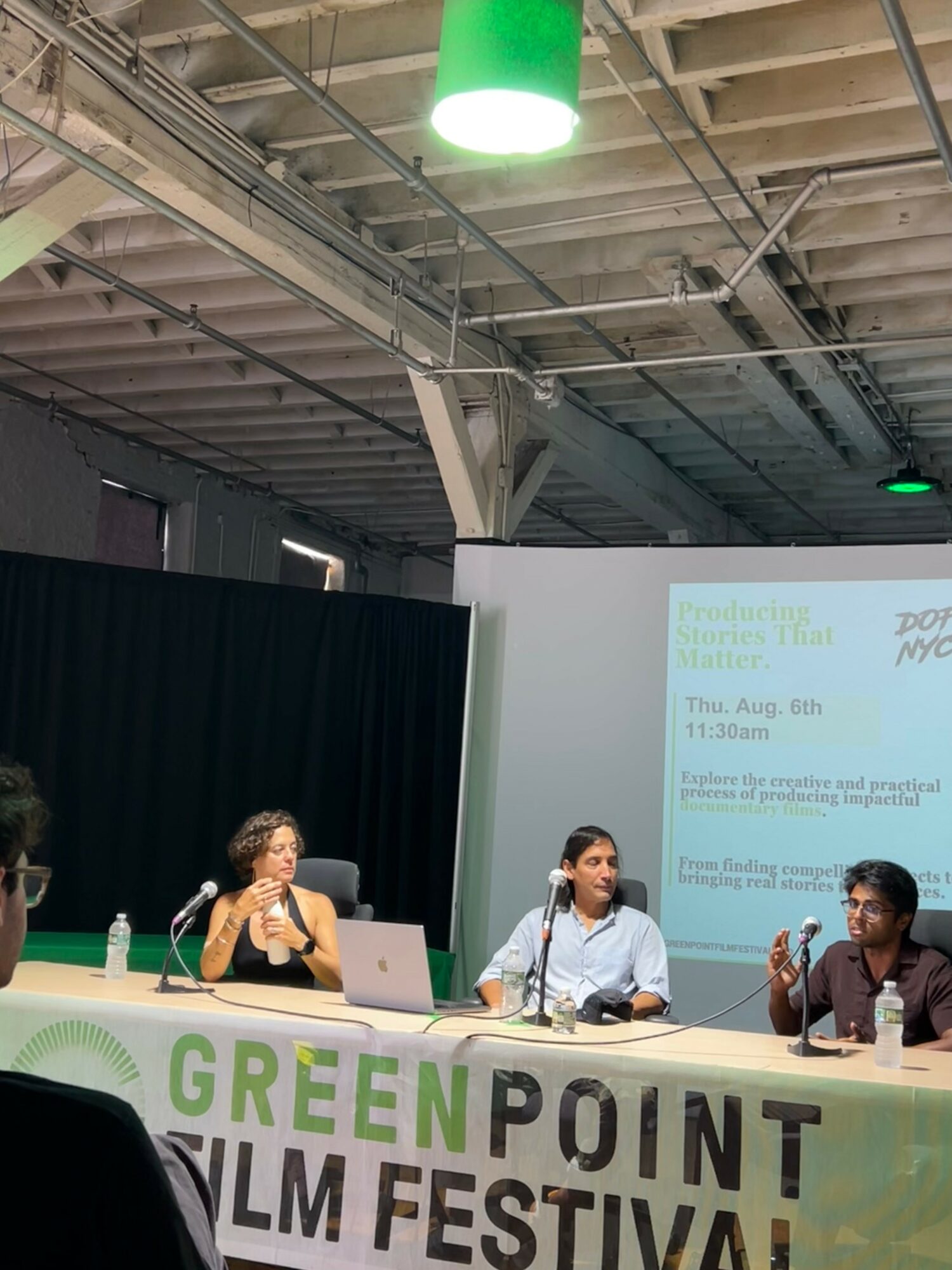 Three people sit at a panel table with a green and white banner reading 'GREEN POINT FILM FESTIVAL' in front, inside a large industrial space.