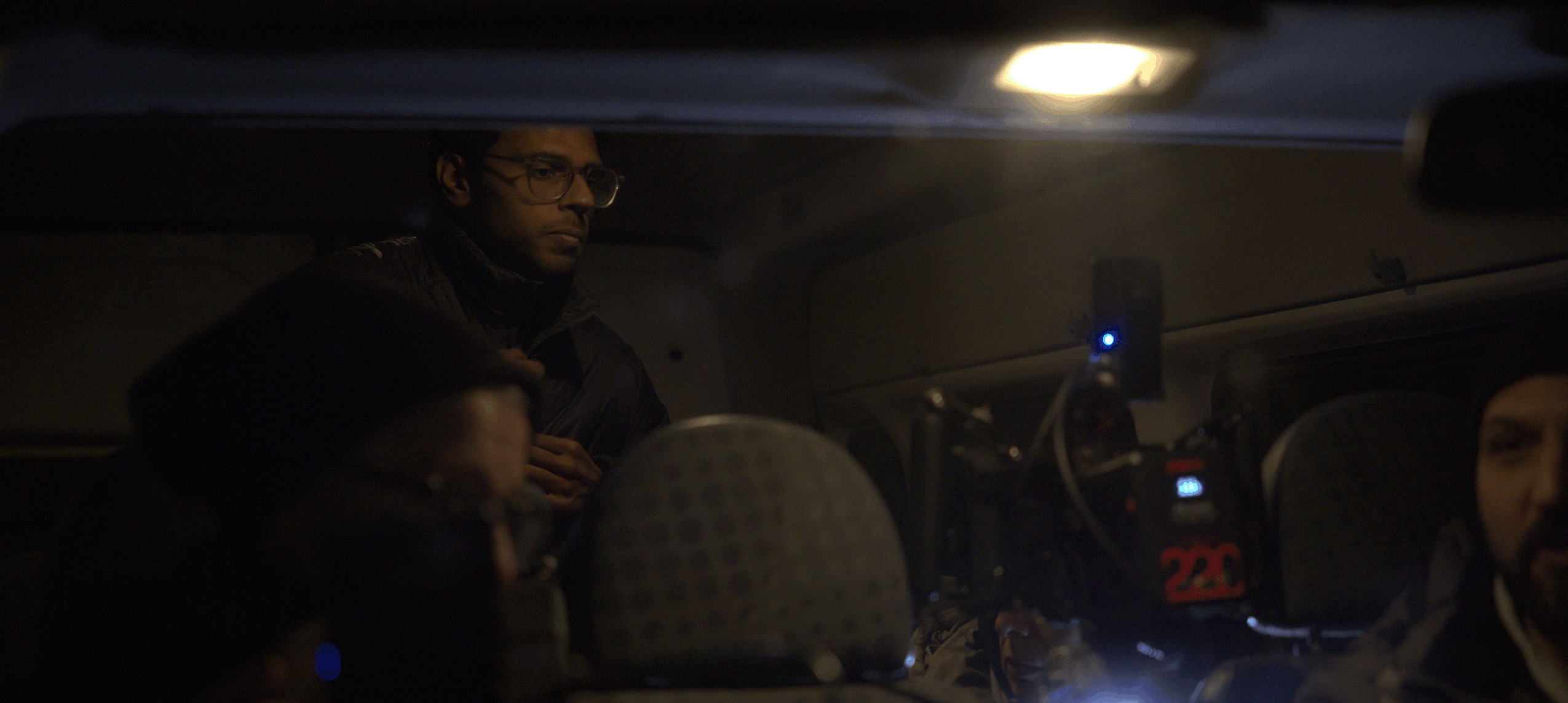 People sitting inside a vehicle at night, with a person standing and a light overhead.