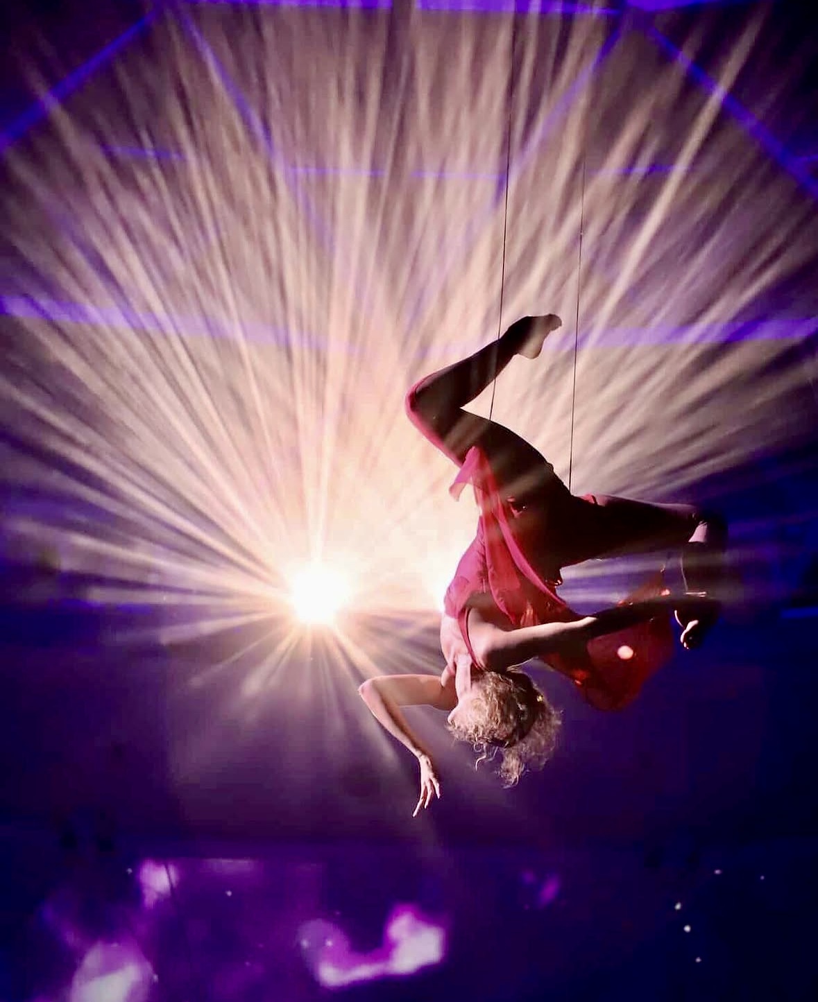A person performing a flip with a bright light and colorful rays in the background.