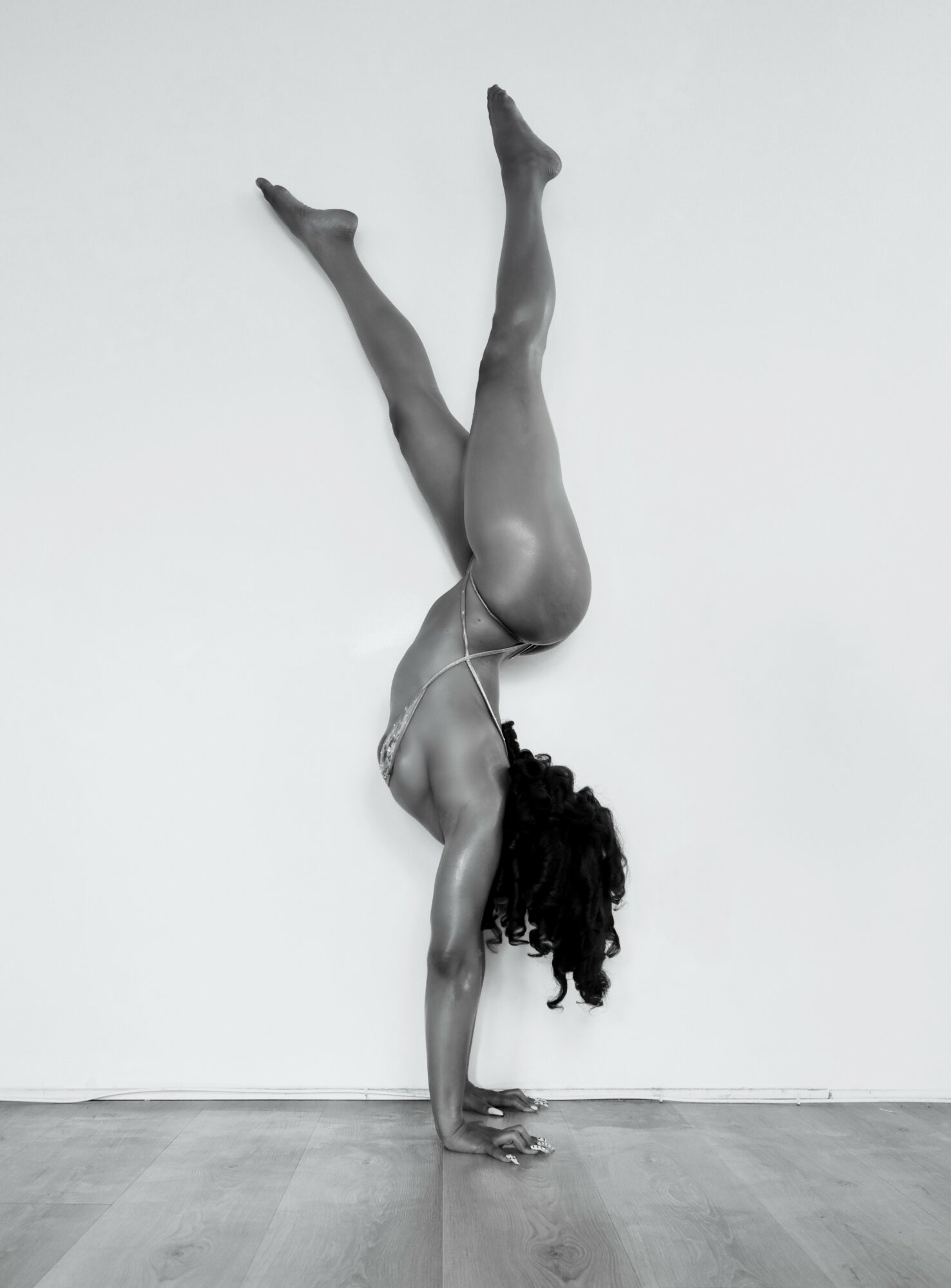 Person performing a handstand against a wall with legs extended upward, in a black and white photo.