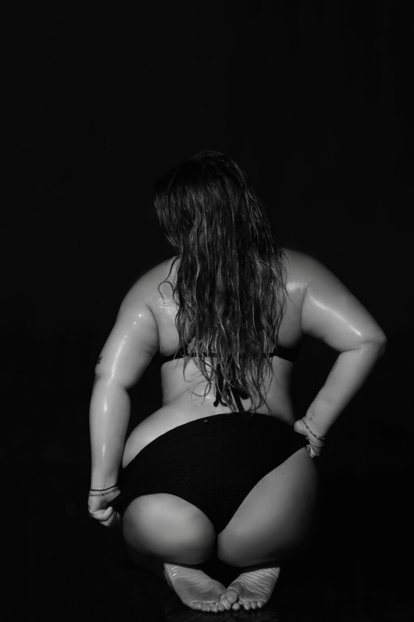 Person with long hair kneeling, back facing camera, in a dark setting.