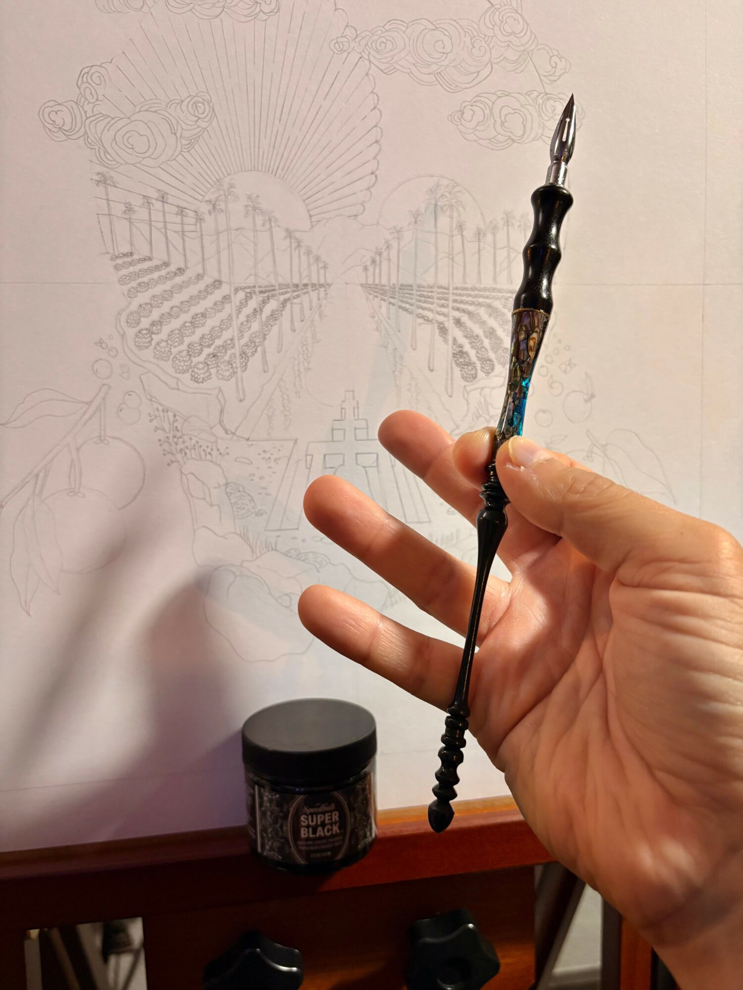 Hand holding a paintbrush with a black handle and metal tip, in front of a wall with faint sketches.