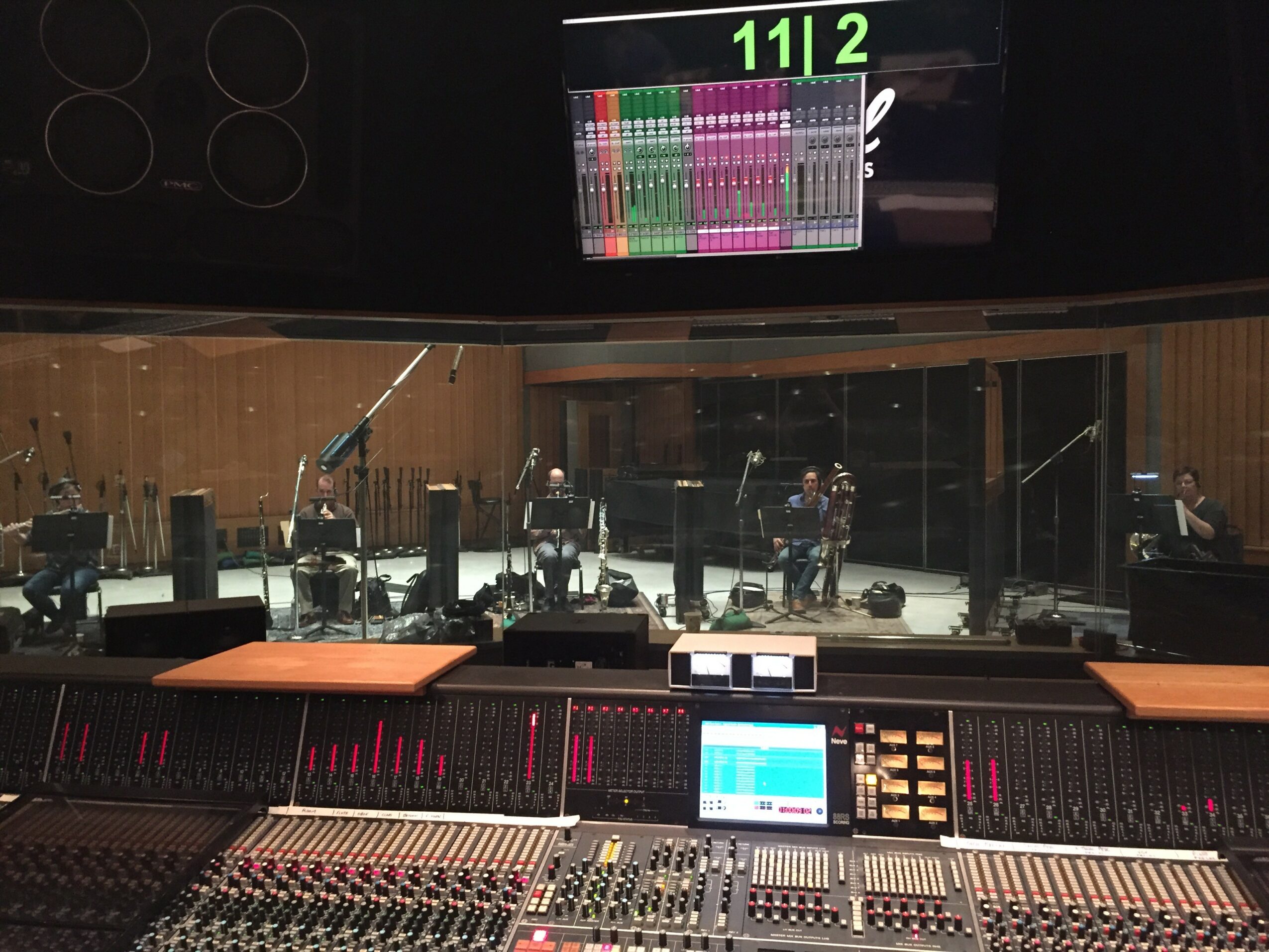 Recording studio with musicians playing instruments, sound mixing console, and a large display screen showing audio levels.