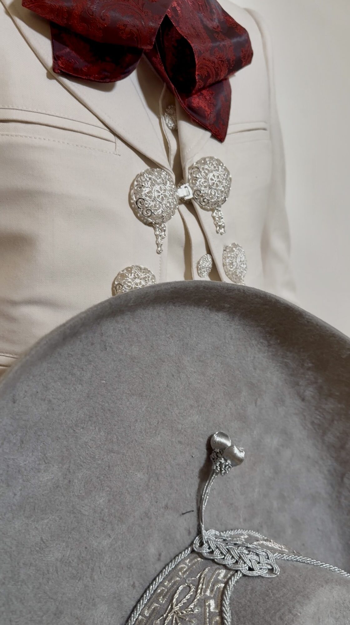 Close-up of a person wearing a white outfit with decorative silver buttons and a red scarf, holding a gray circular object.