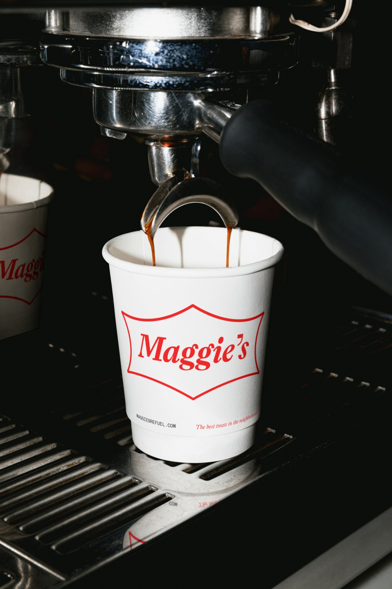 Espresso machine pouring coffee into a Maggie's branded cup, with another cup nearby, on a metal drip tray.
