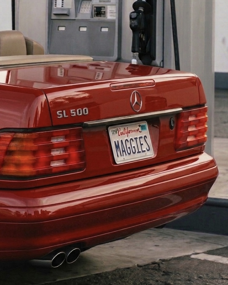Red Mercedes-Benz SL 500 with California license plate reading MAGGIES, parked near a building with a gas pump in the background.