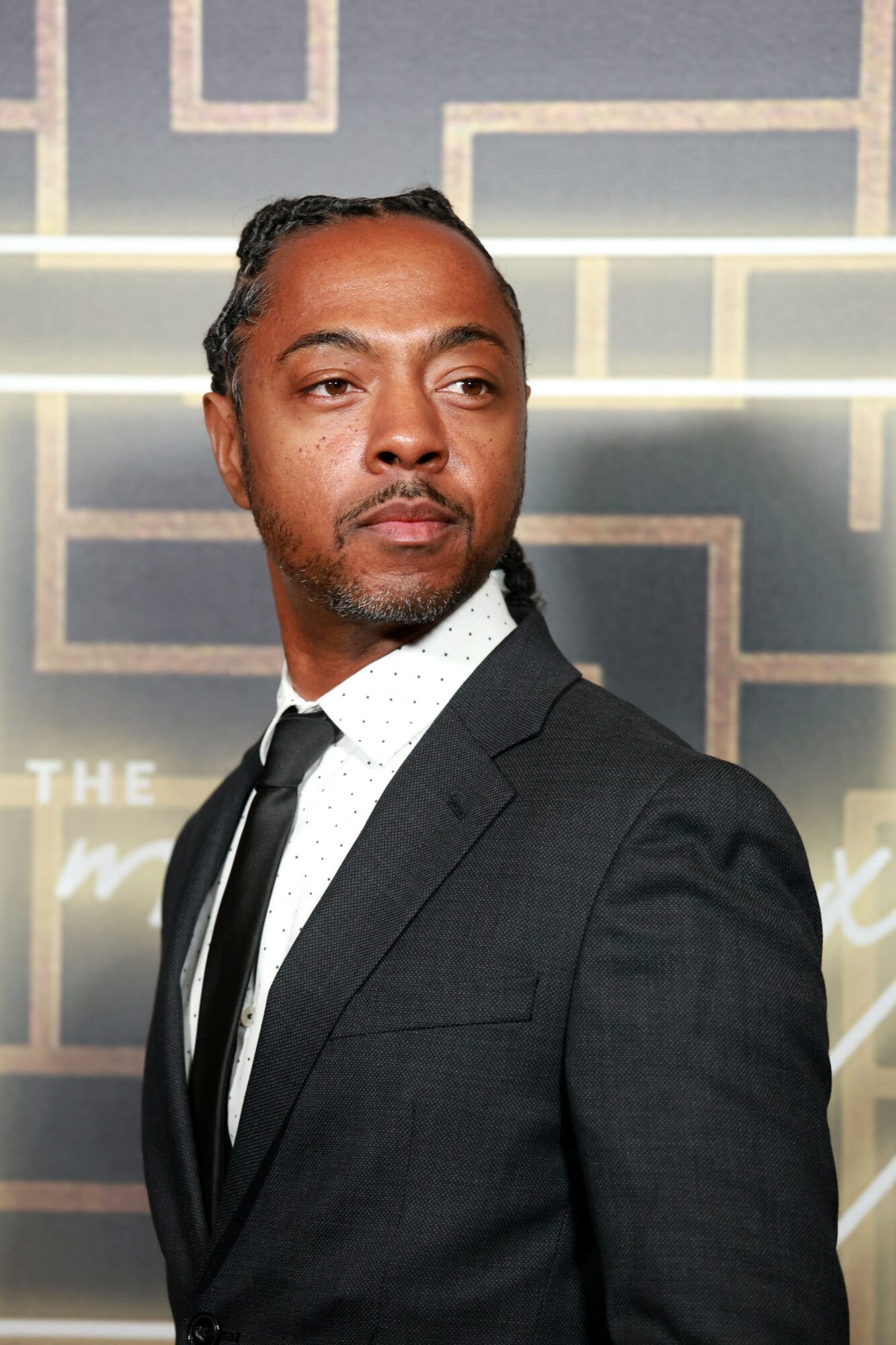 Man in a suit looking to the side with a geometric background behind him.