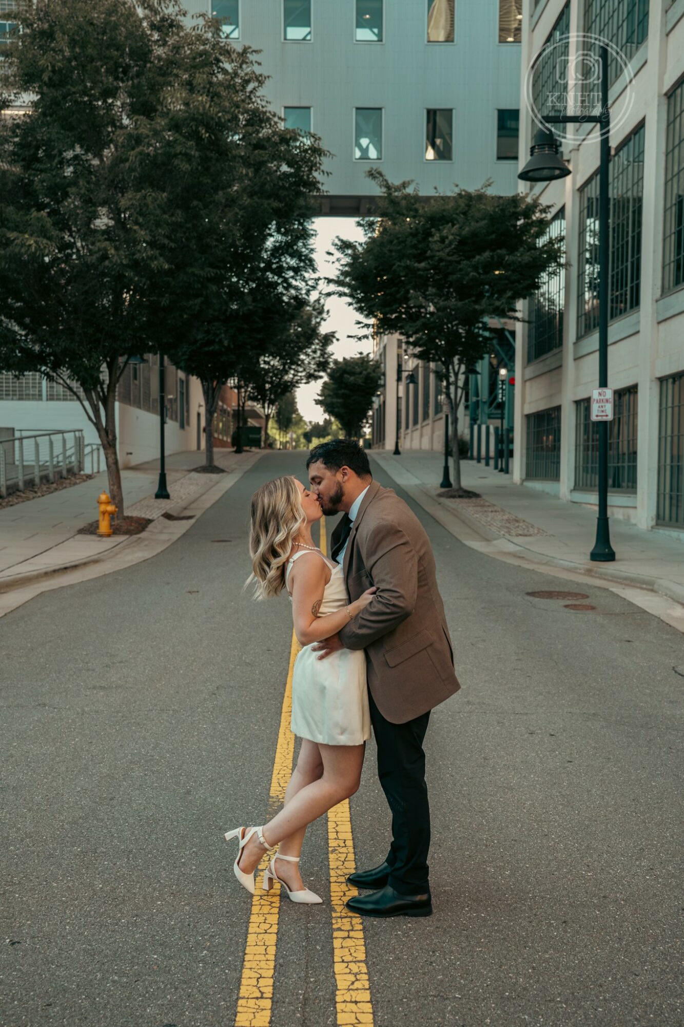 A couple stands close together in the middle of a city street, holding hands and looking at each other.