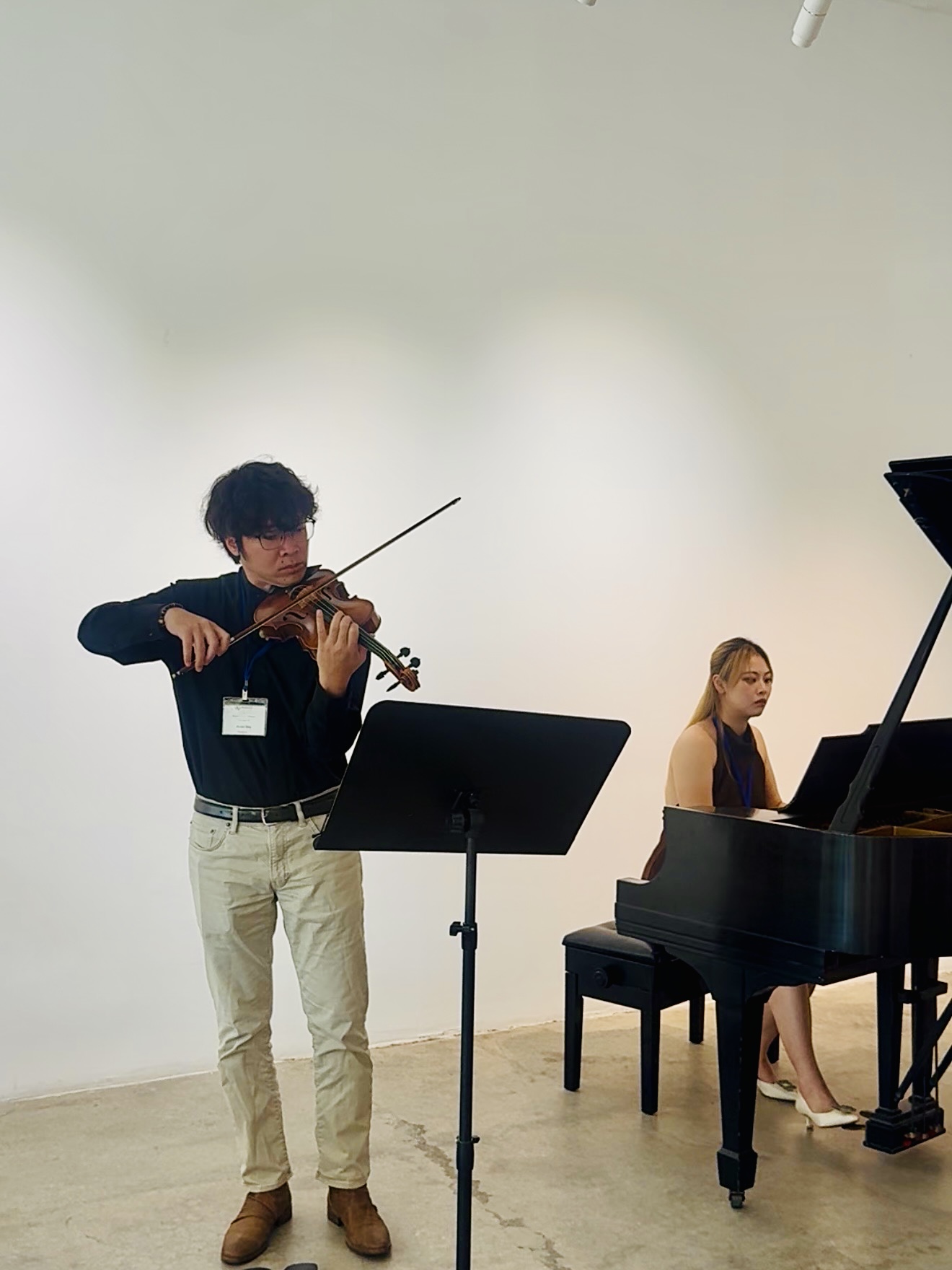A young man playing violin and a young woman at a piano in a room with plain white walls.
