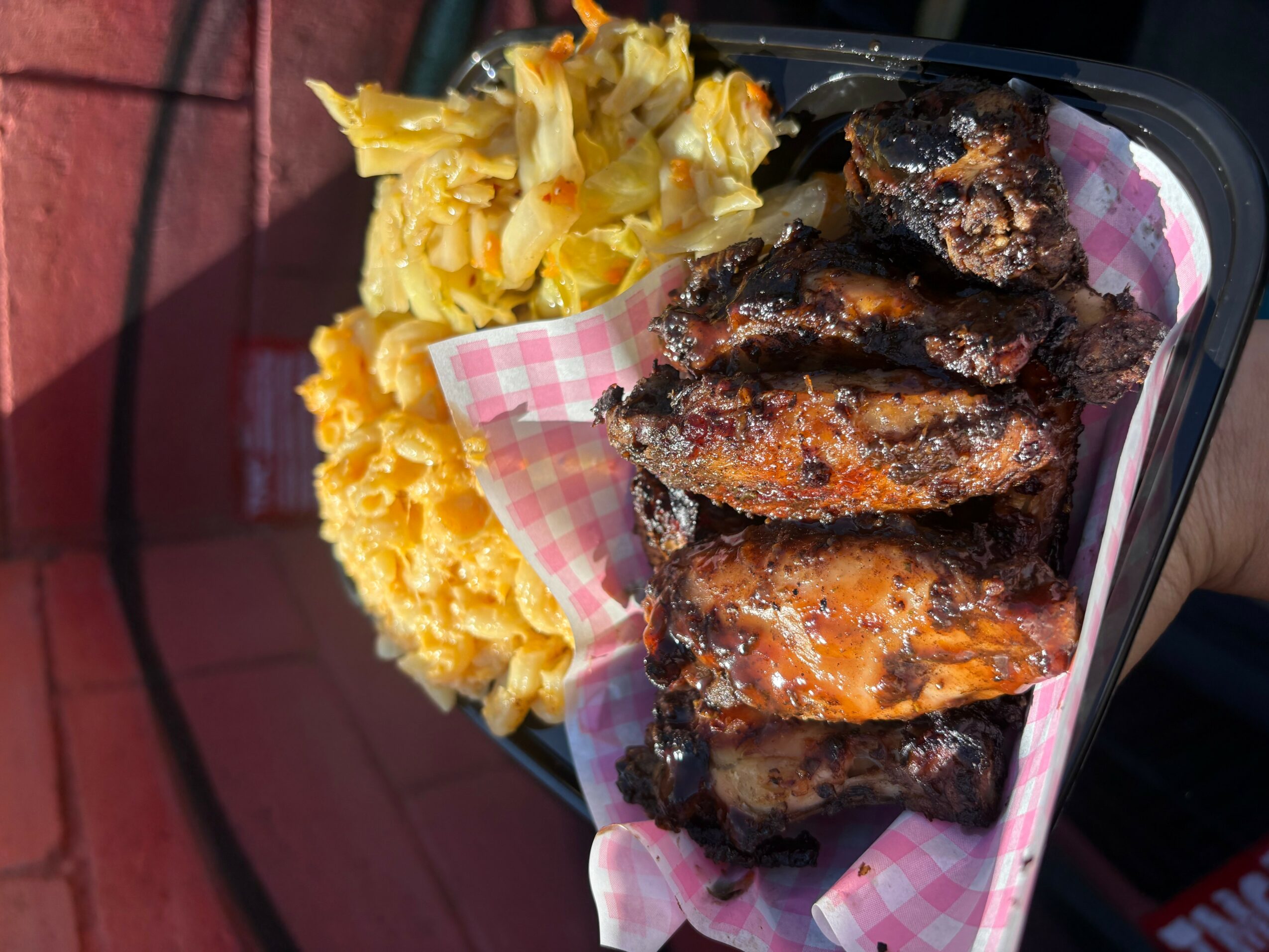 Barbecue ribs with sides of potato salad and macaroni and cheese on a tray, outdoors.