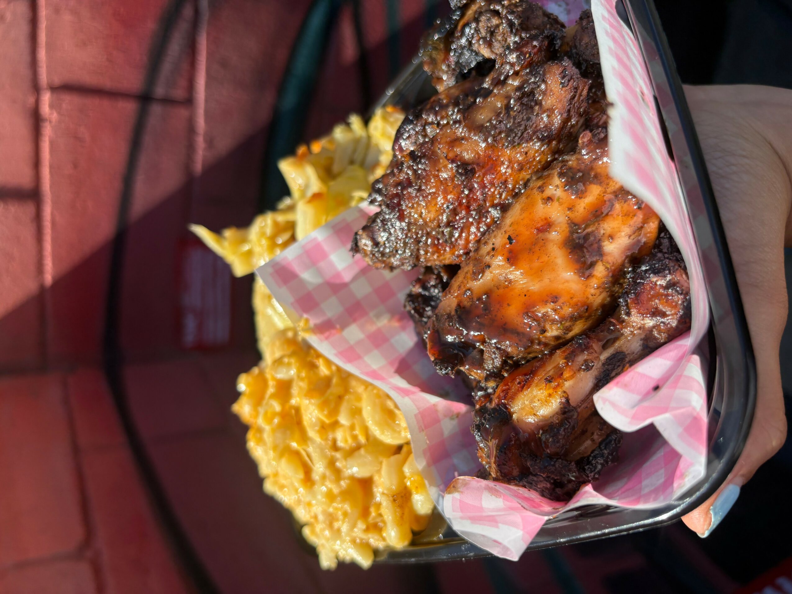 Person holding a basket with fried chicken and a side of yellow macaroni and cheese, lined with pink checkered paper.