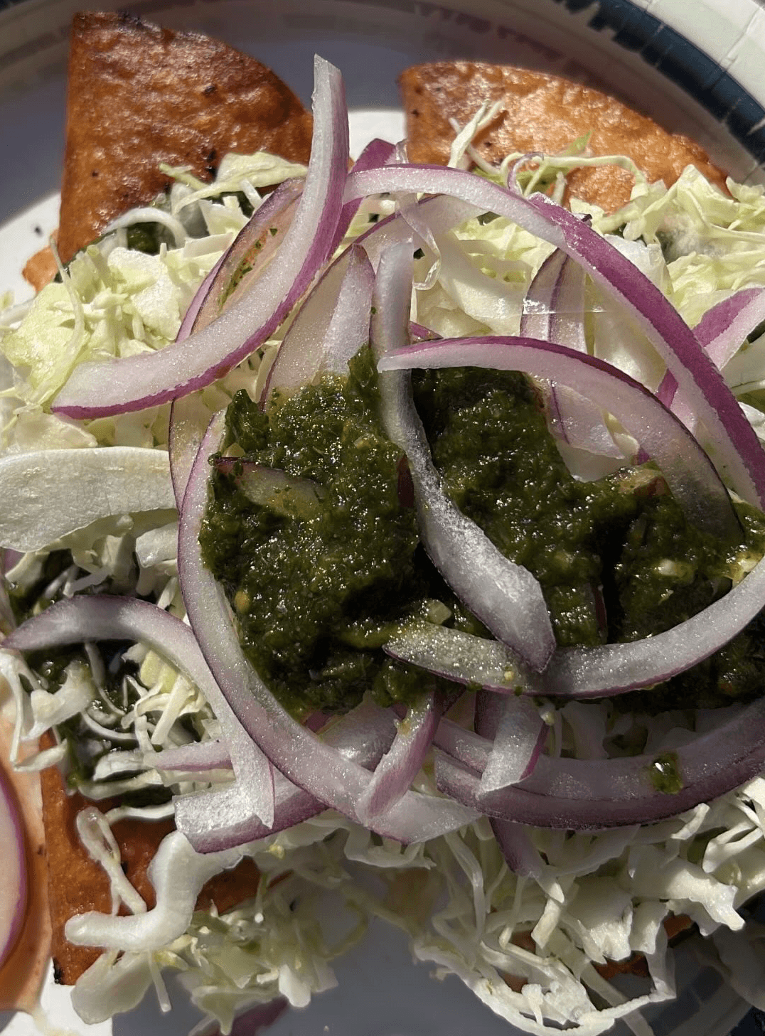 Salad with shredded cabbage, sliced red onions, green sauce, and fried items on a plate.