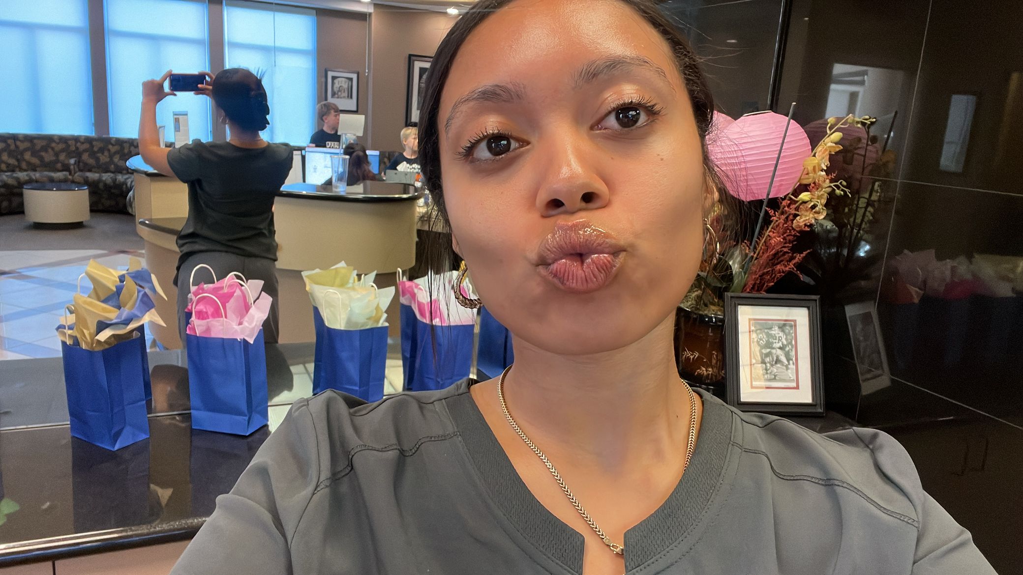 Woman taking a selfie at a celebration with colorful decorations and a table with gifts in the background.