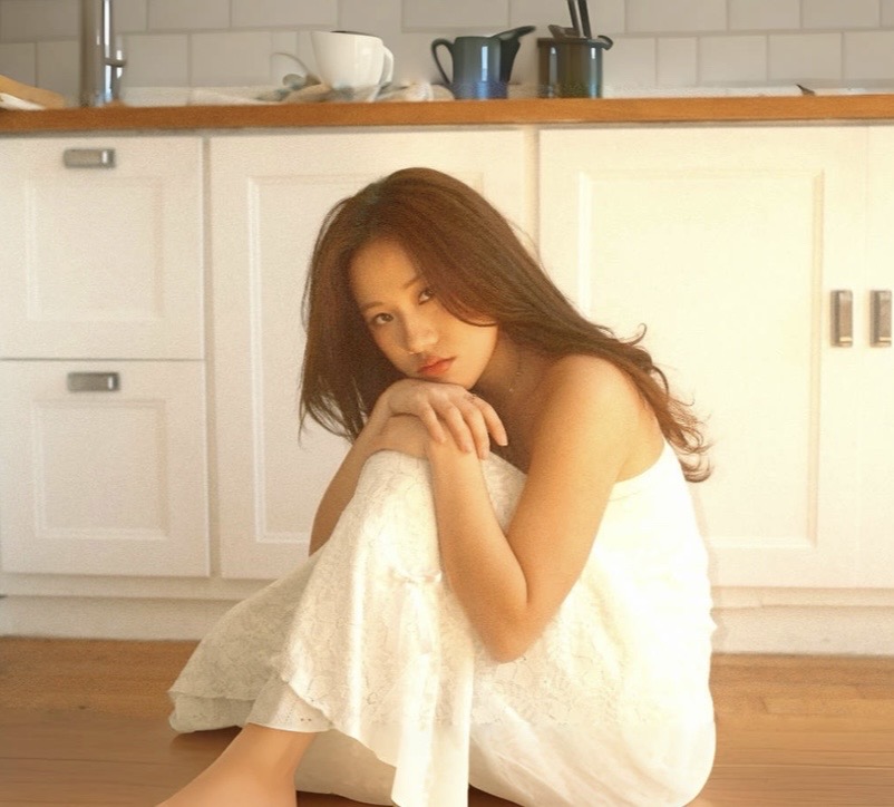 Young woman sitting on the floor in a kitchen, wrapped in a white towel, looking at the camera.