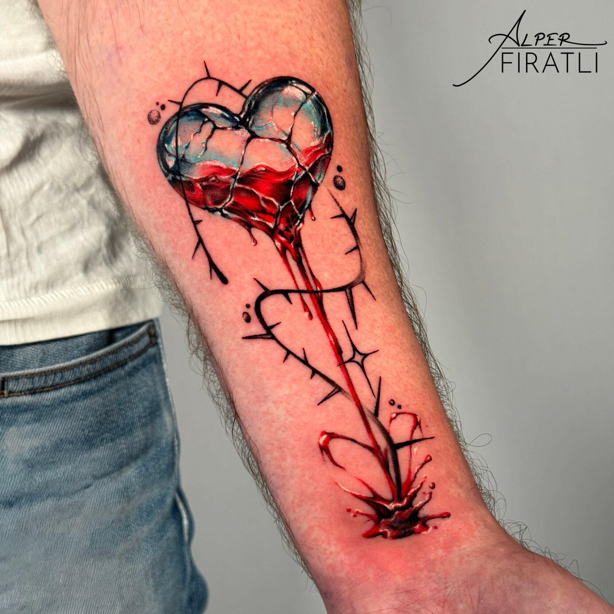 Tattoo of a broken heart with a bleeding line extending downward, surrounded by black ink accents on forearm.