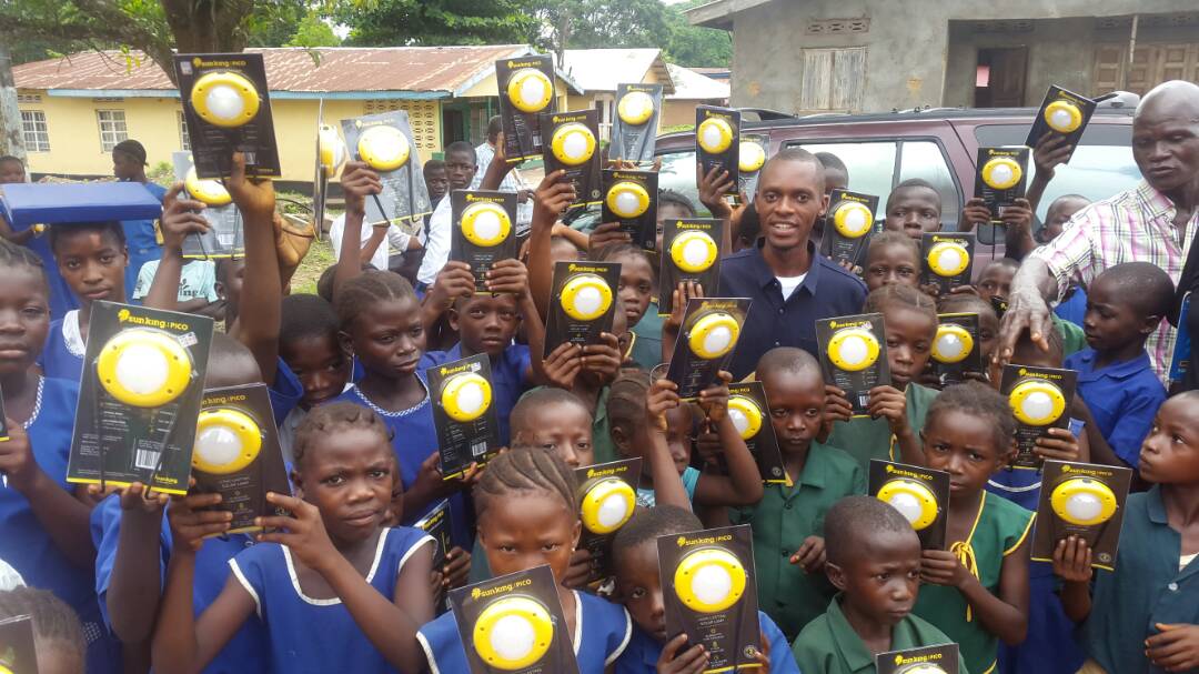 Group of children and adults holding yellow and black flashlights outdoors, some smiling and looking at the camera.