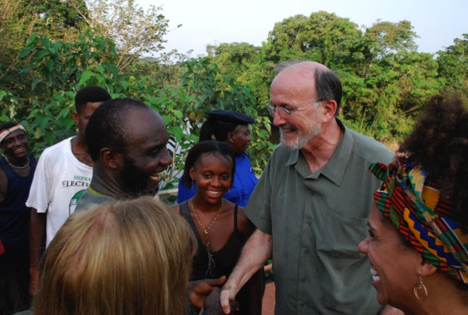 Group of people outdoors smiling and talking, with trees in the background.