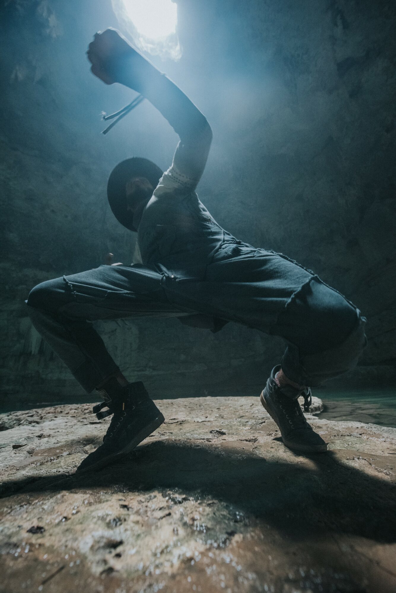 Person crouching with one arm raised in a dark, misty environment with light shining from above.
