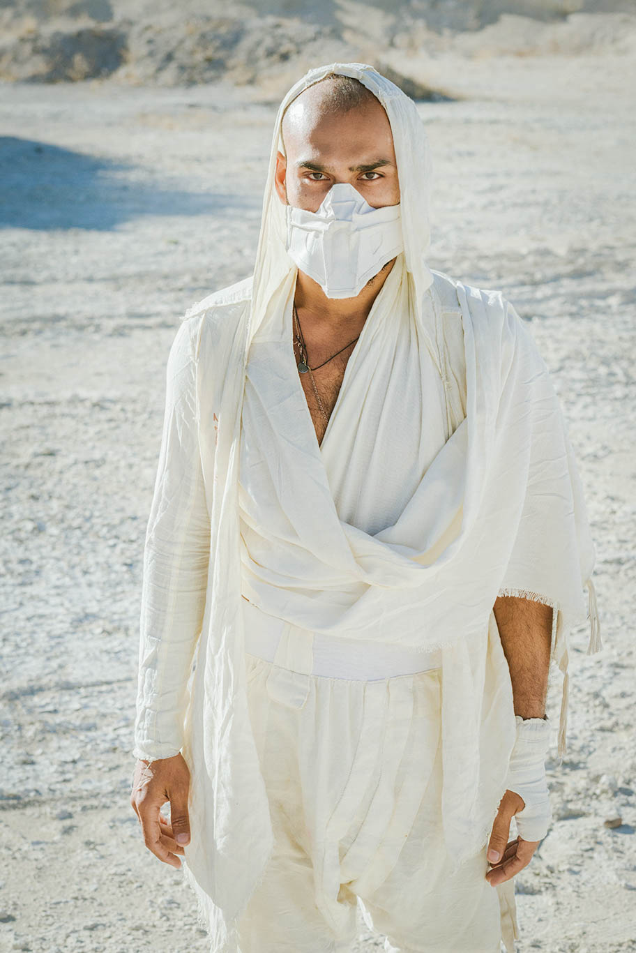 Person wearing a white outfit and face mask outdoors, with a sandy or desert background.