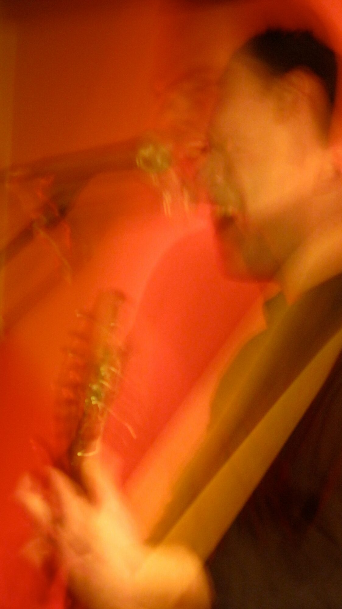 Blurry image of a person playing a saxophone in a dimly lit setting.