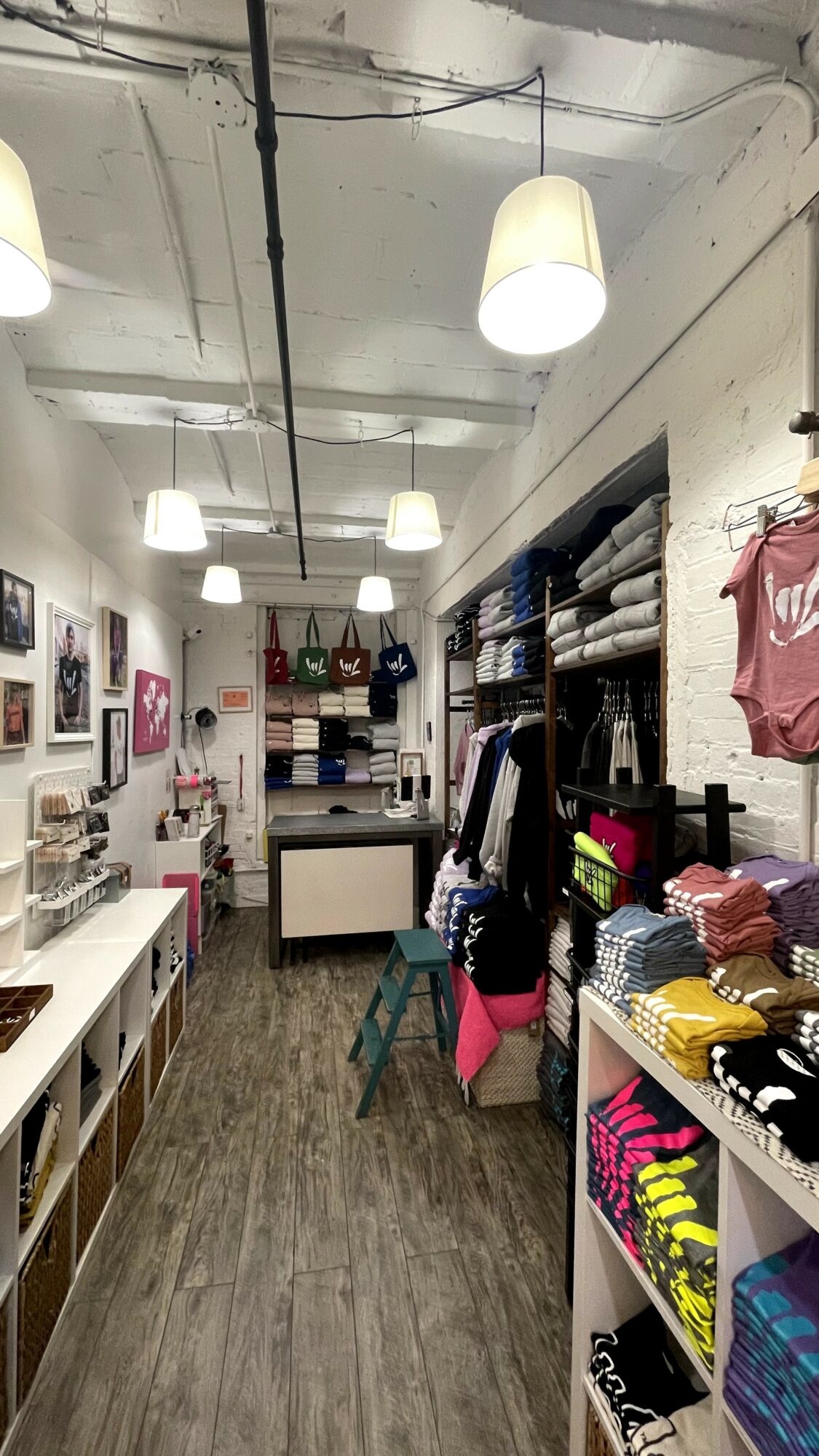 Clothing store interior with shelves of folded clothes, hanging garments, and ceiling lights, viewed from the entrance.