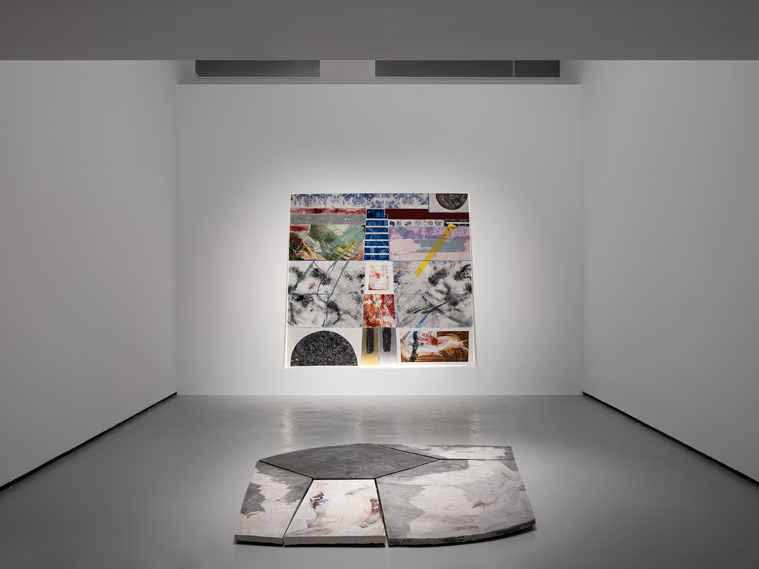 Abstract artwork displayed on a white gallery wall with a large, irregularly shaped sculpture on the floor in front.