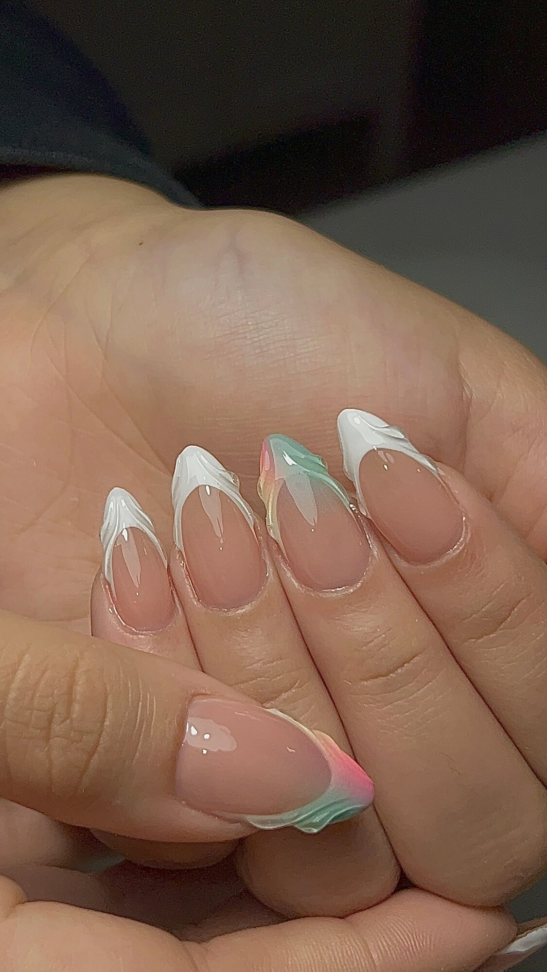 Close-up of a hand with long, decorated nails featuring pastel colors and white tips.