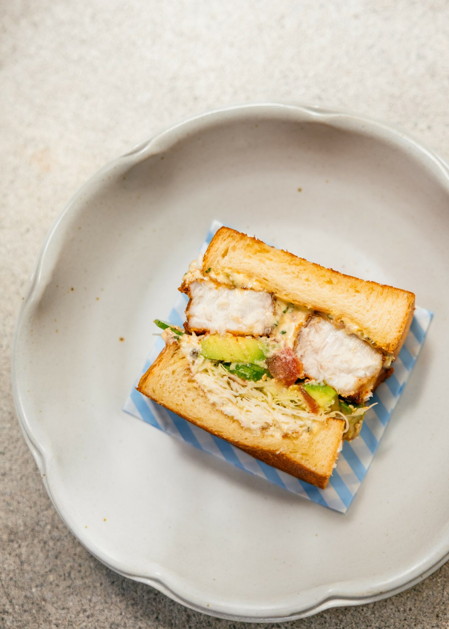 Sandwich with fried chicken, lettuce, and tomato on a white plate, viewed from above.
