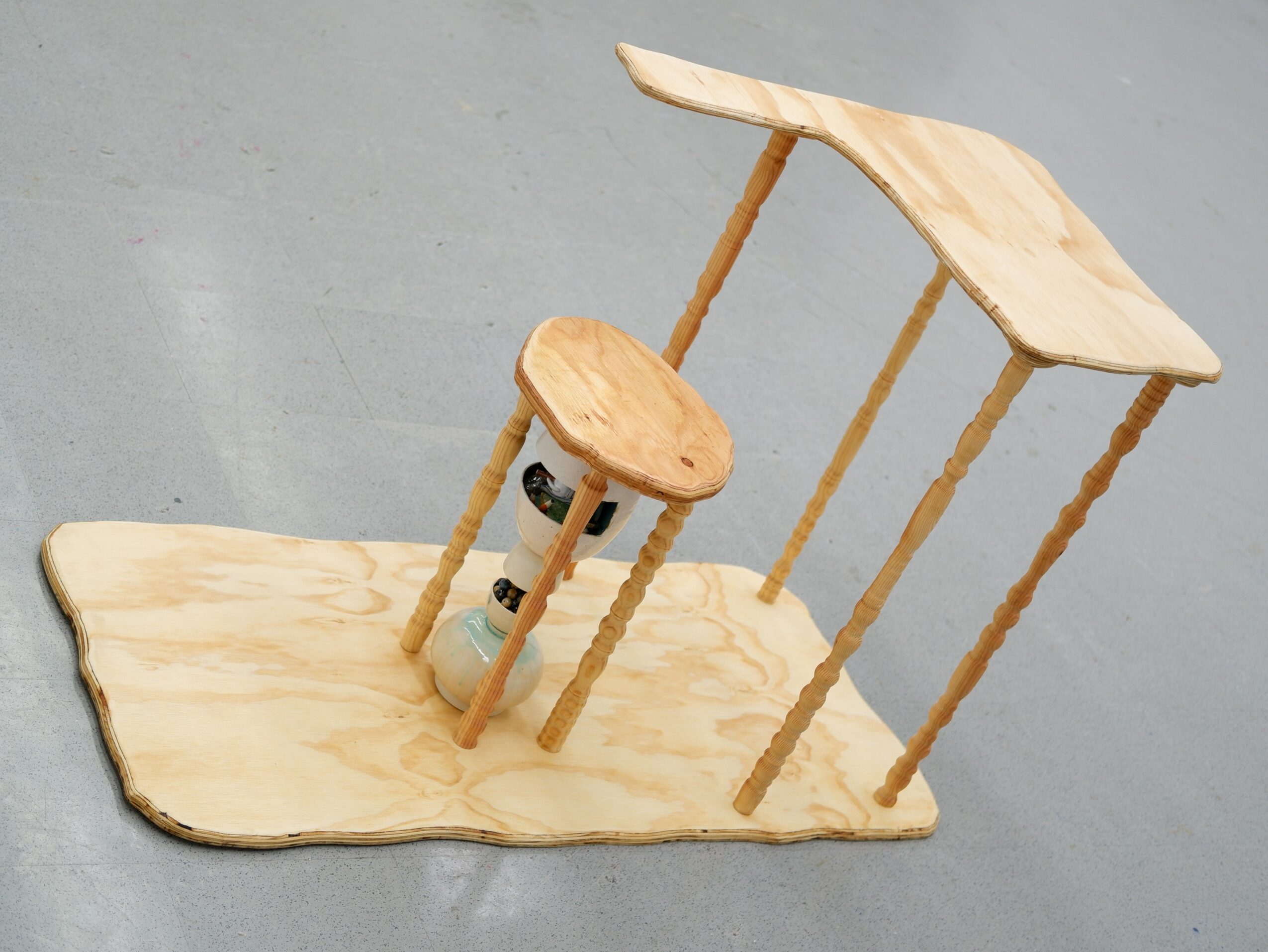 Wooden structure with a flat base, three vertical supports, and a curved top surface, resembling a small table or stand.