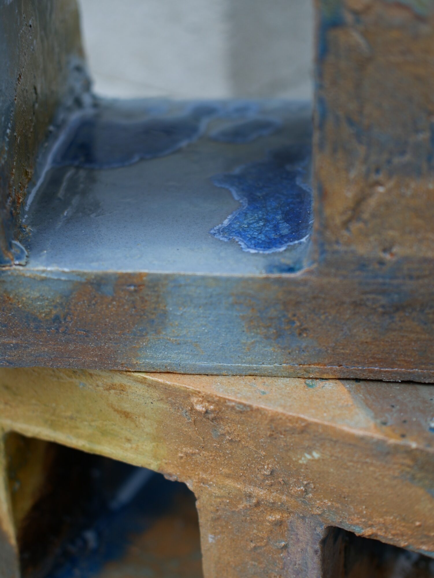 Close-up of a metal surface with water and rust, showing a small puddle and corrosion, with brick and wood in the background.