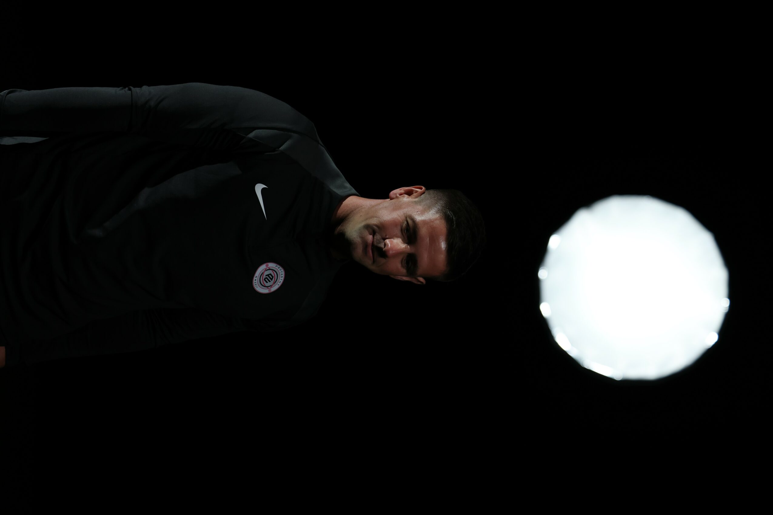 Person in black clothing standing in dark environment with bright light source nearby.