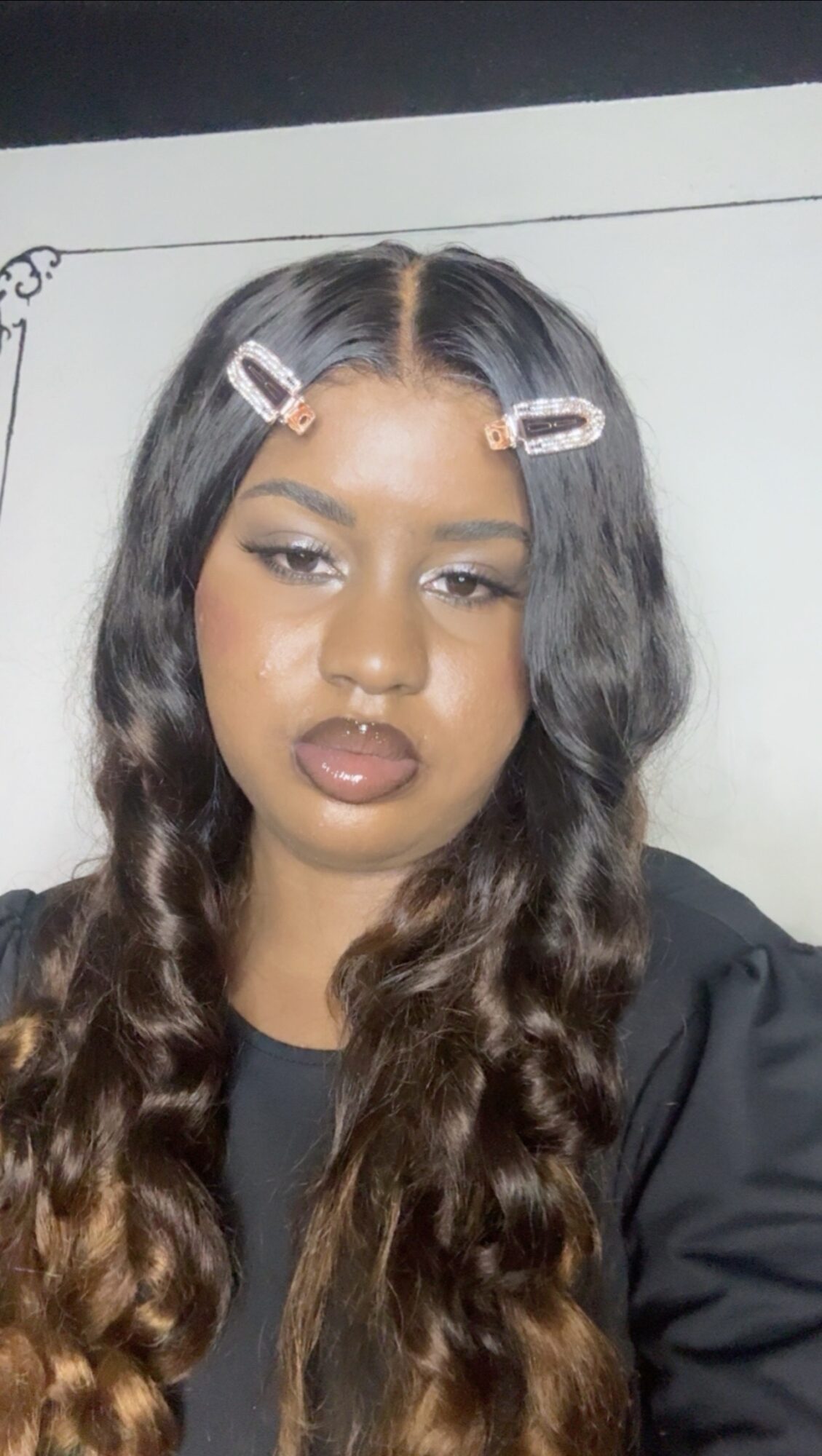 Young woman with long wavy hair, hair clips, and makeup, looking at the camera.