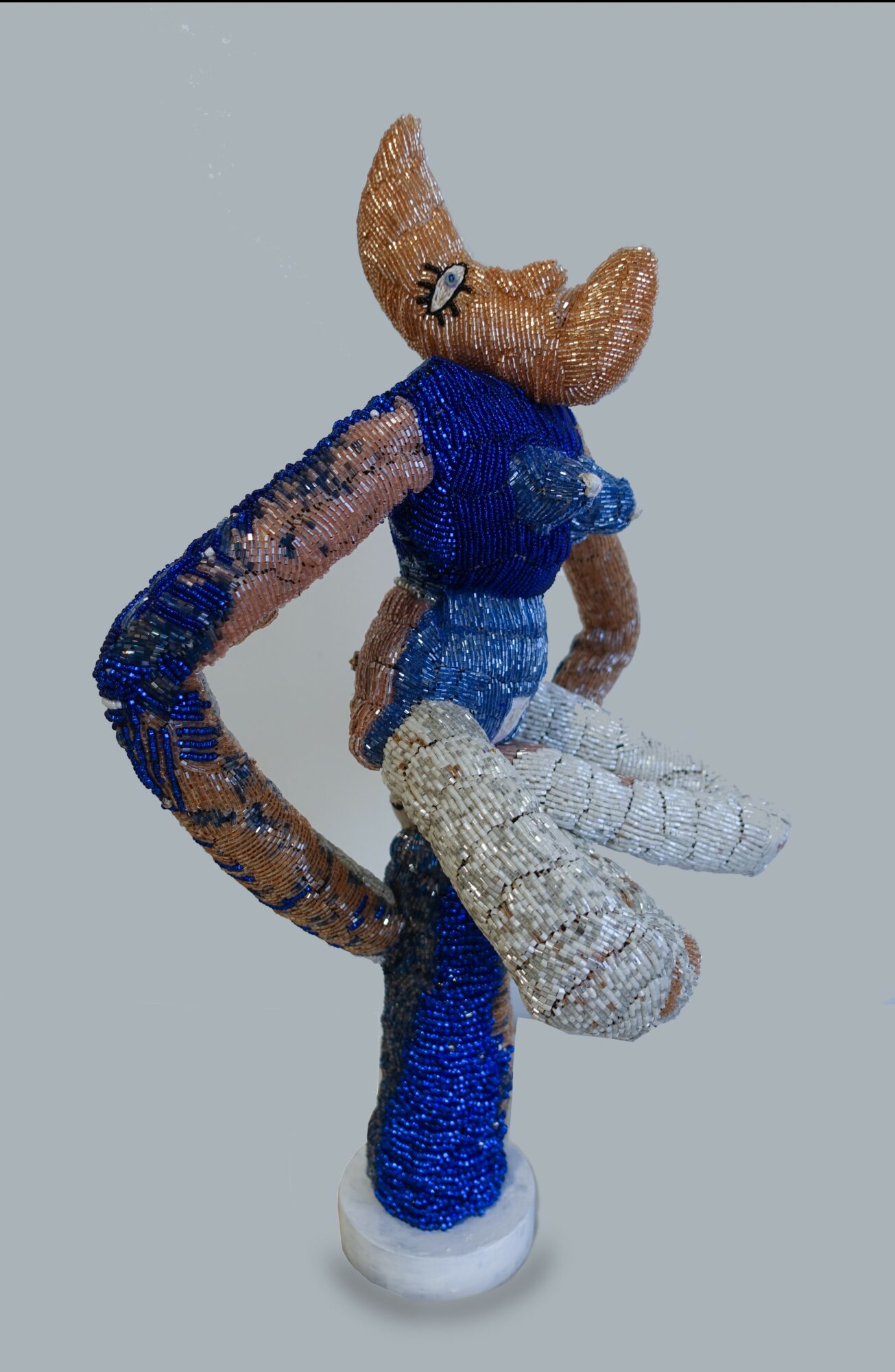 A plush toy character with a large head, wearing a blue shirt and white pants, standing on a white surface.