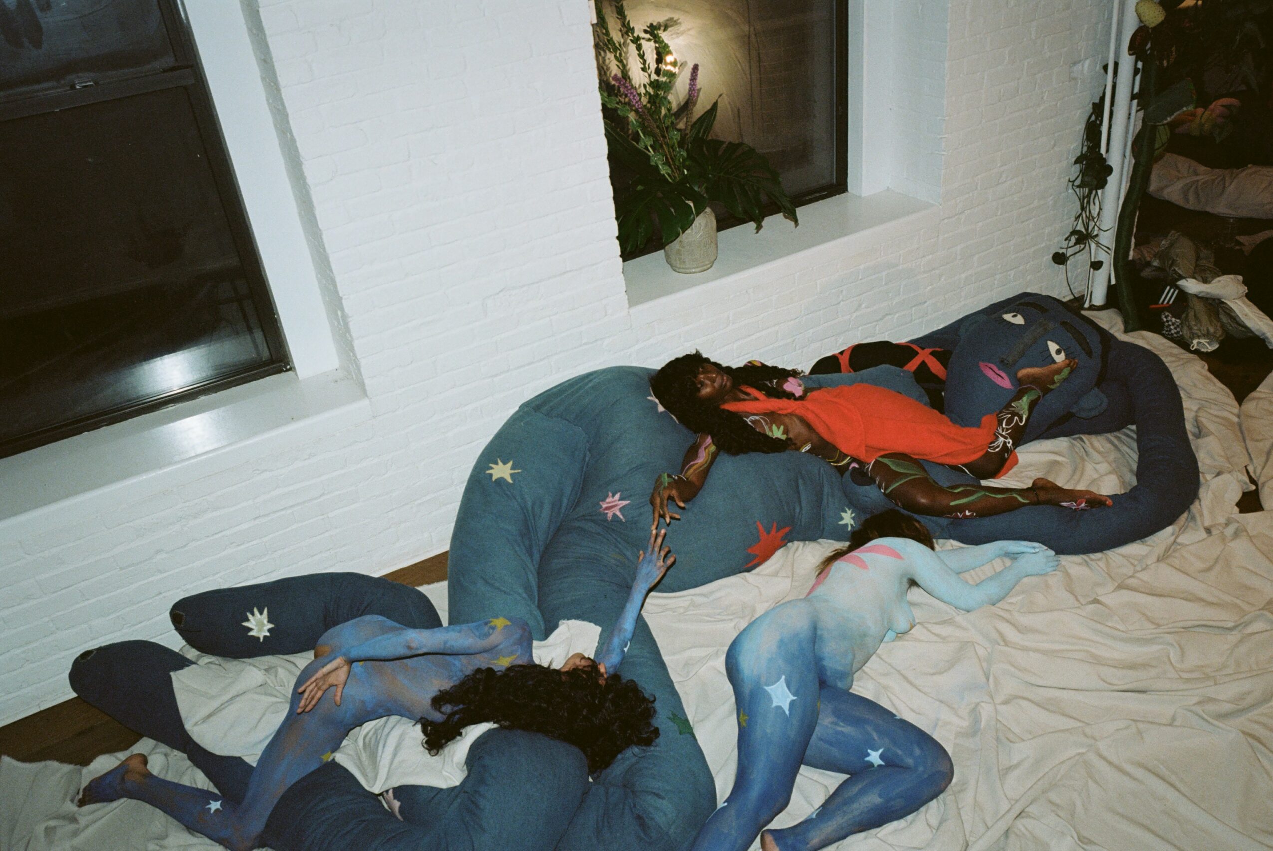 Two people lying on the floor, one in blue pajamas and the other in dark clothing, near a window with a plant. Word count: 20