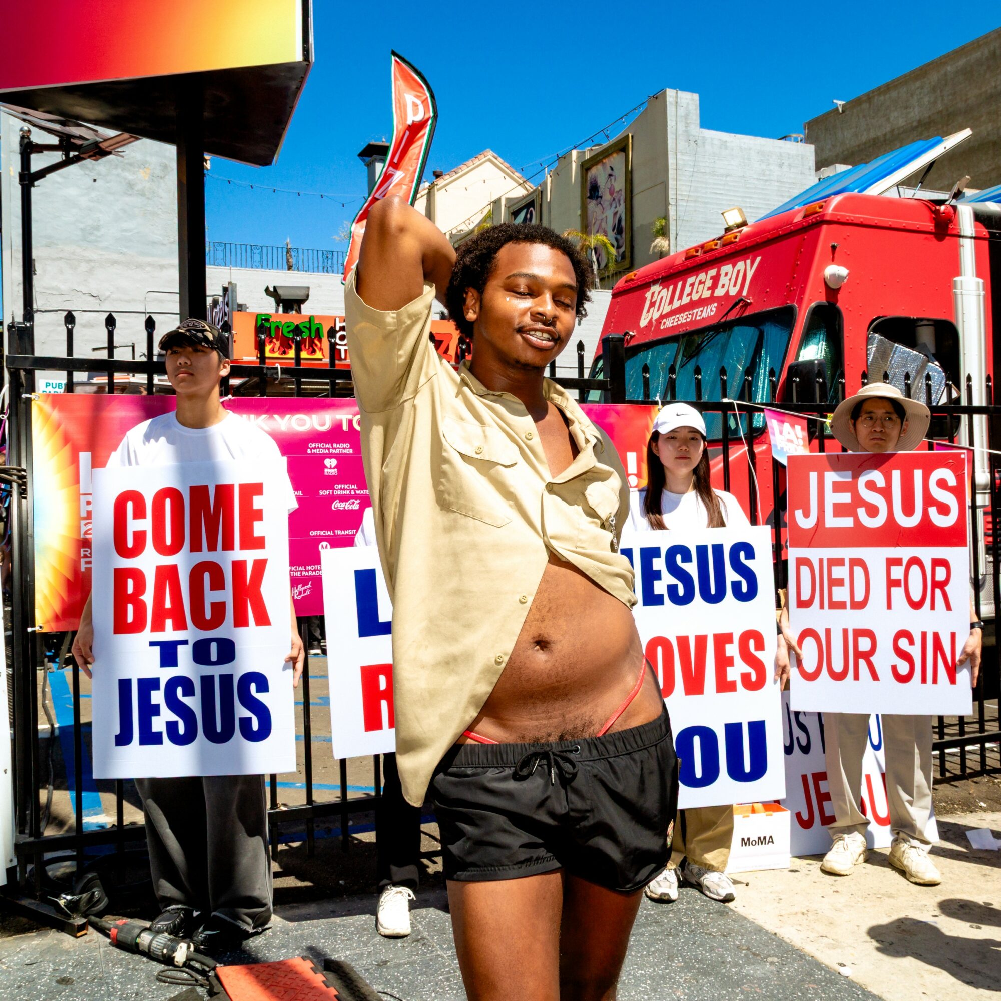 Smiling woman with raised hand standing in front of protest signs about Jesus and salvation, sunny day, urban background.