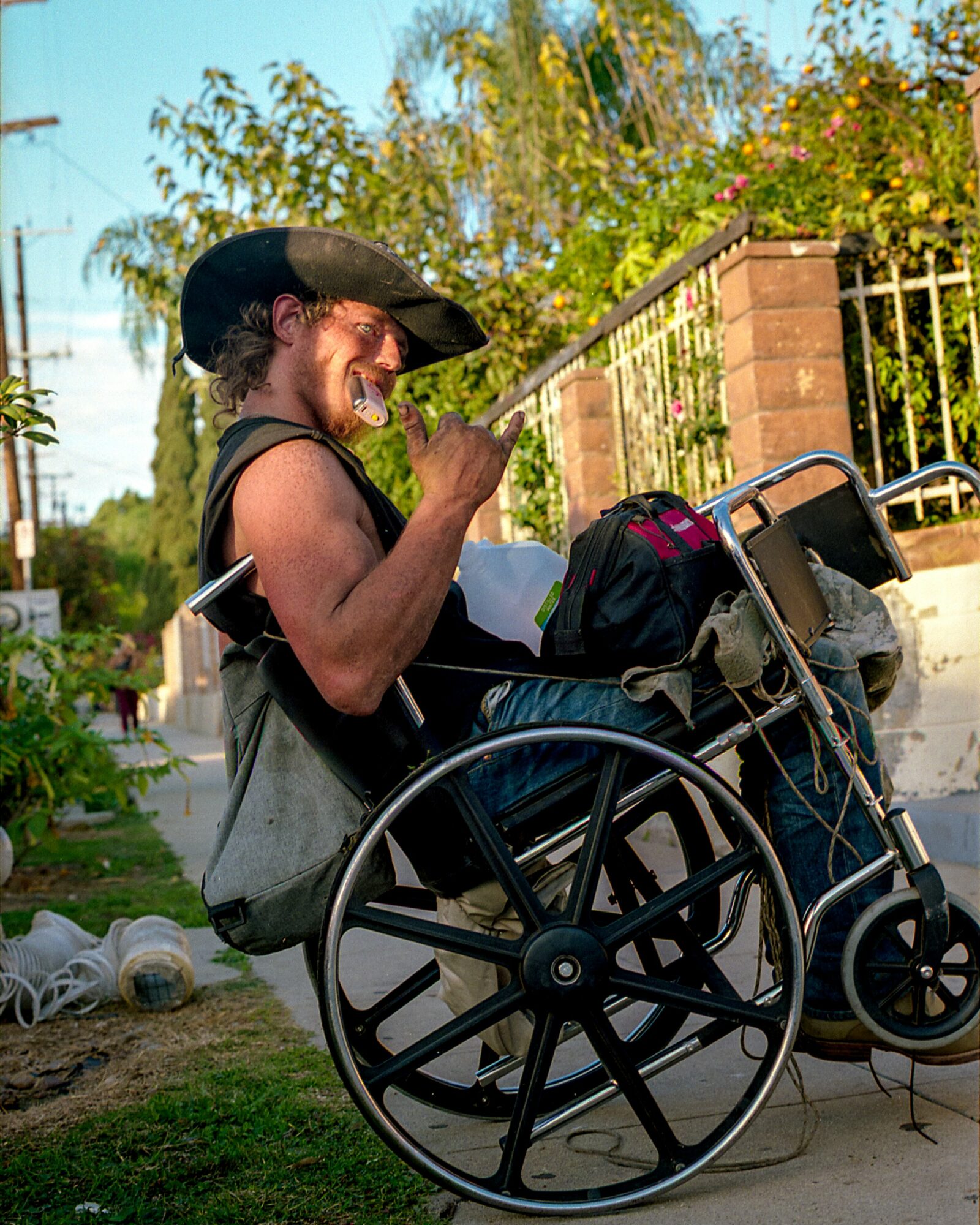Person in a wheelchair smiling and playing guitar outdoors with trees and a fence in the background.