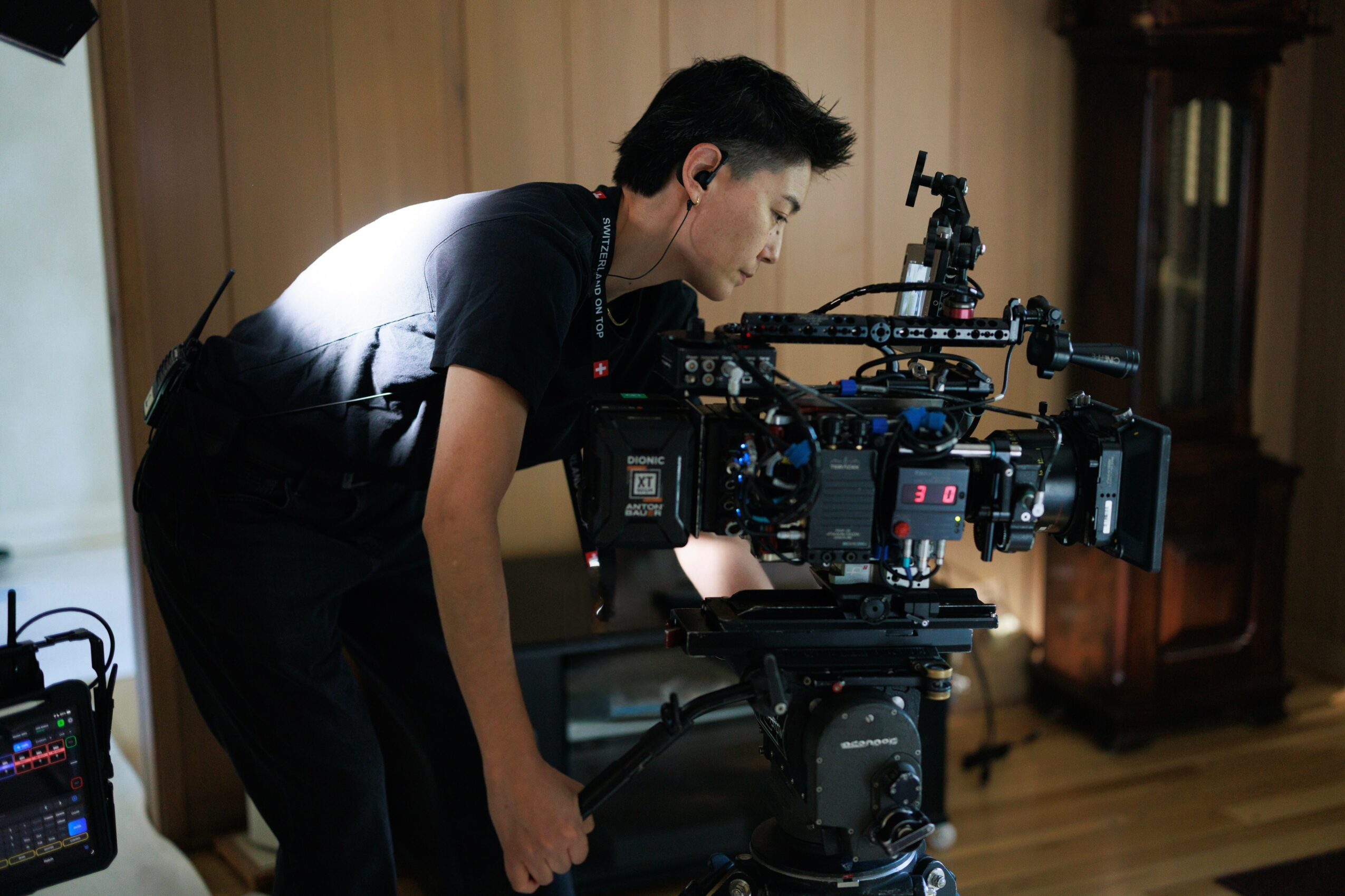 Person operating a professional camera on a tripod indoors, with a wooden cabinet in the background.