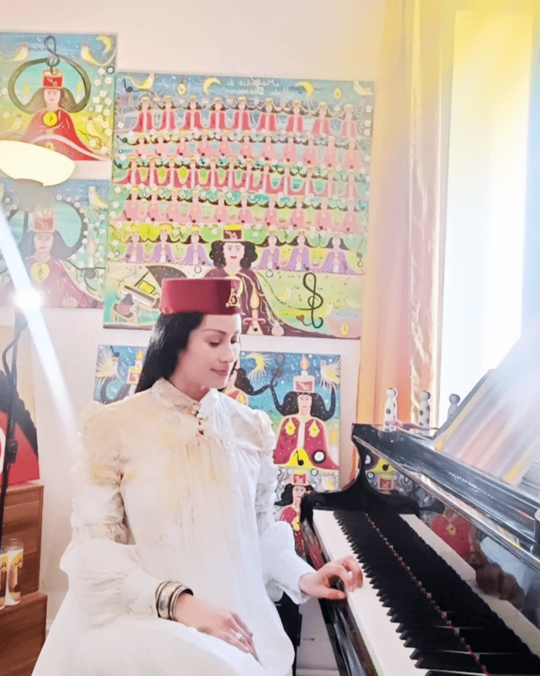Woman playing piano in a room with colorful posters on the wall, sunlight coming through a window.