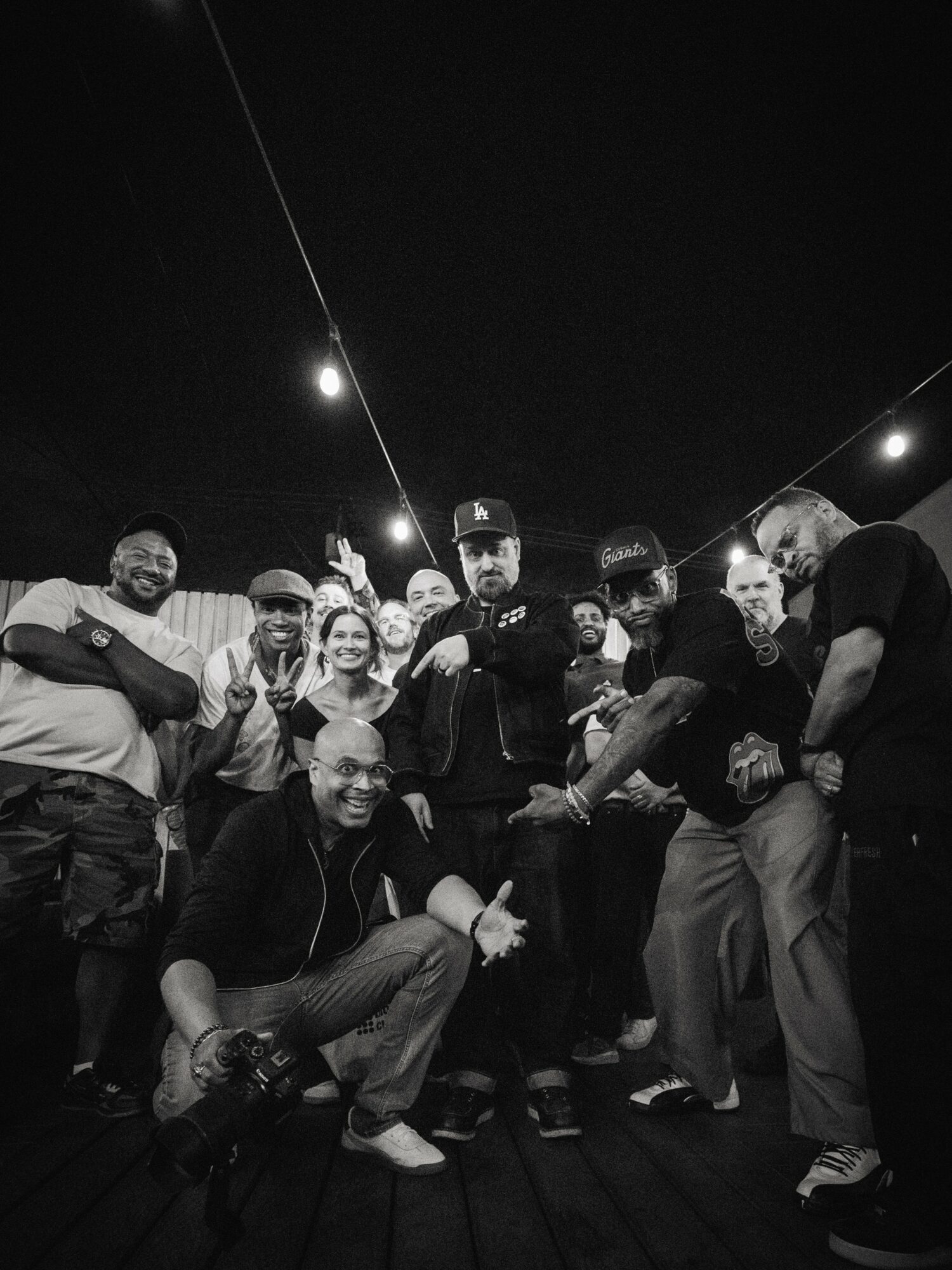 Group of people smiling and posing together outdoors at night, with string lights overhead.